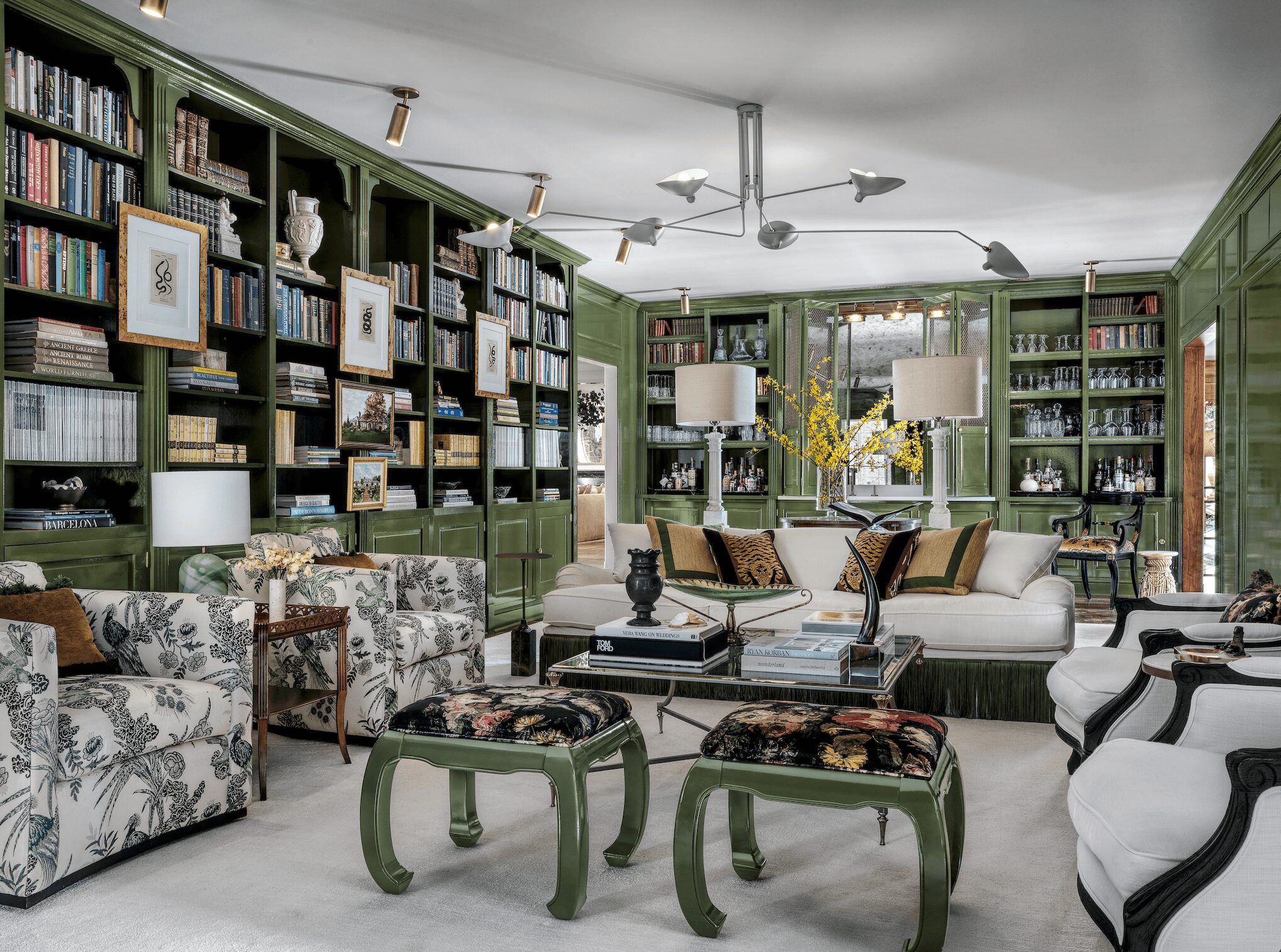 Living room with green bookshelves, sofas, armchairs, lamps, and decorative items, arranged in a cozy, elegant setting.