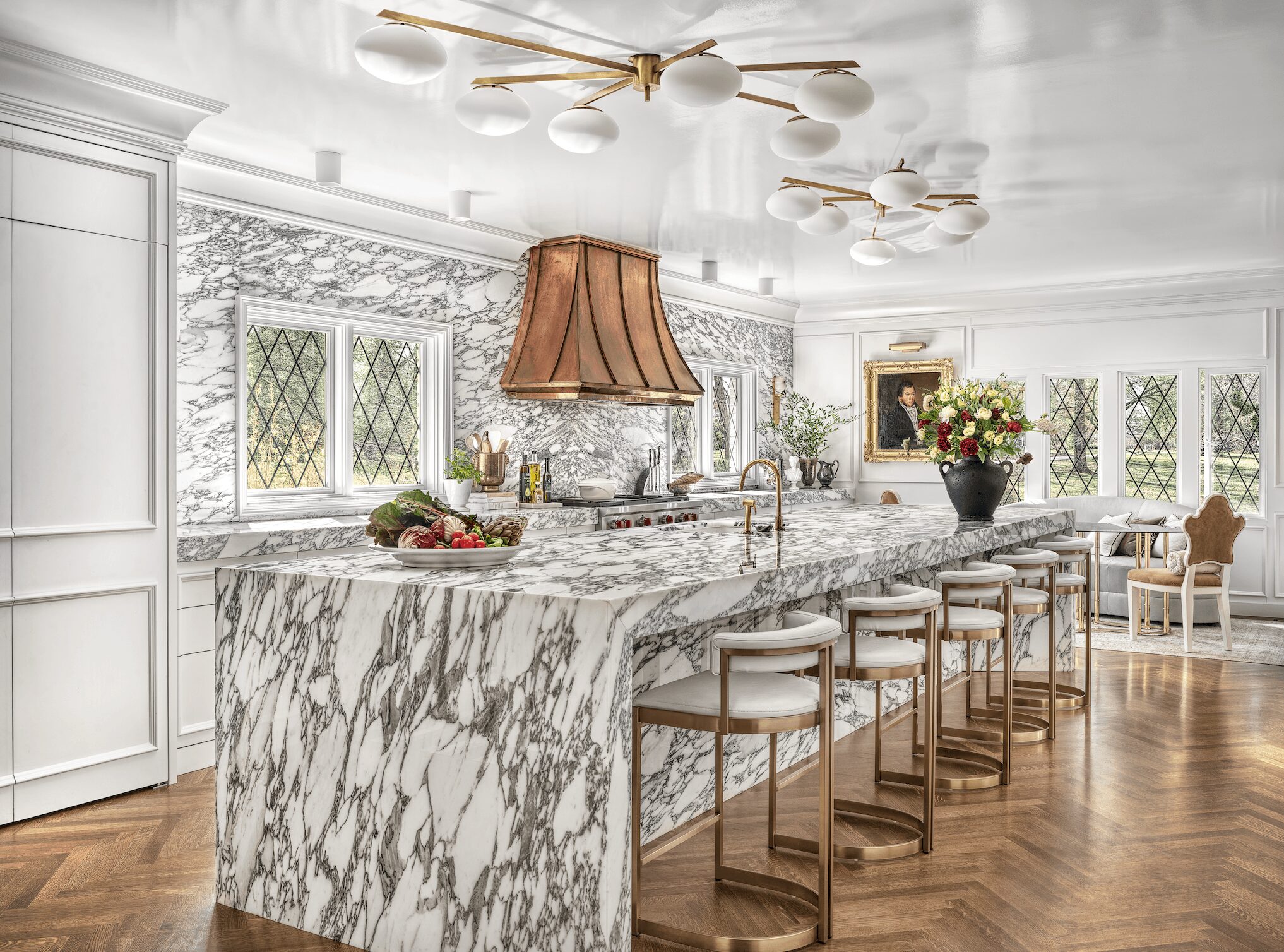 Bright kitchen with marble island, white cabinets, and large windows with diamond-patterned glass.