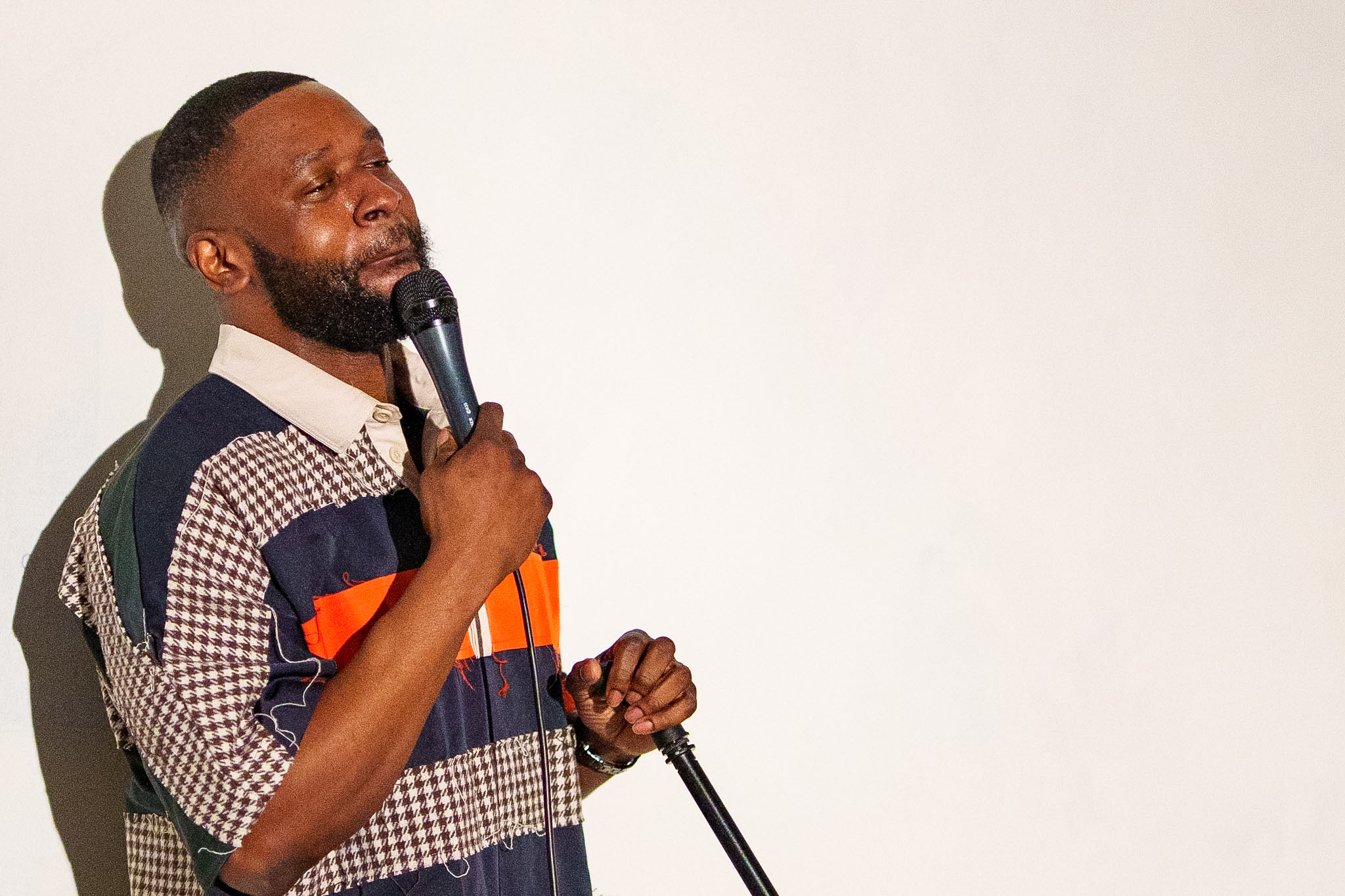 Person holding a microphone, speaking or performing, with a plain white background.