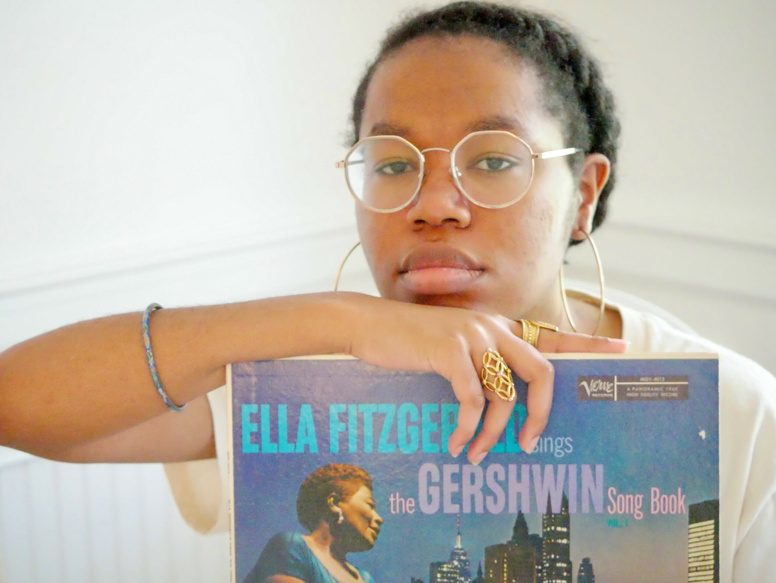 Young woman with glasses and hoop earrings resting her arm on a book about Ella Fitzgerald and the Gershwin songbook.
