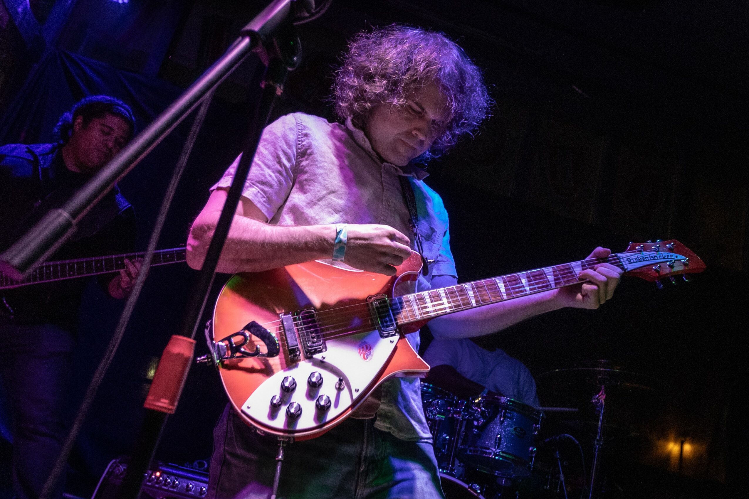 Person with curly hair playing an electric guitar on stage, with a dark background and stage lighting.