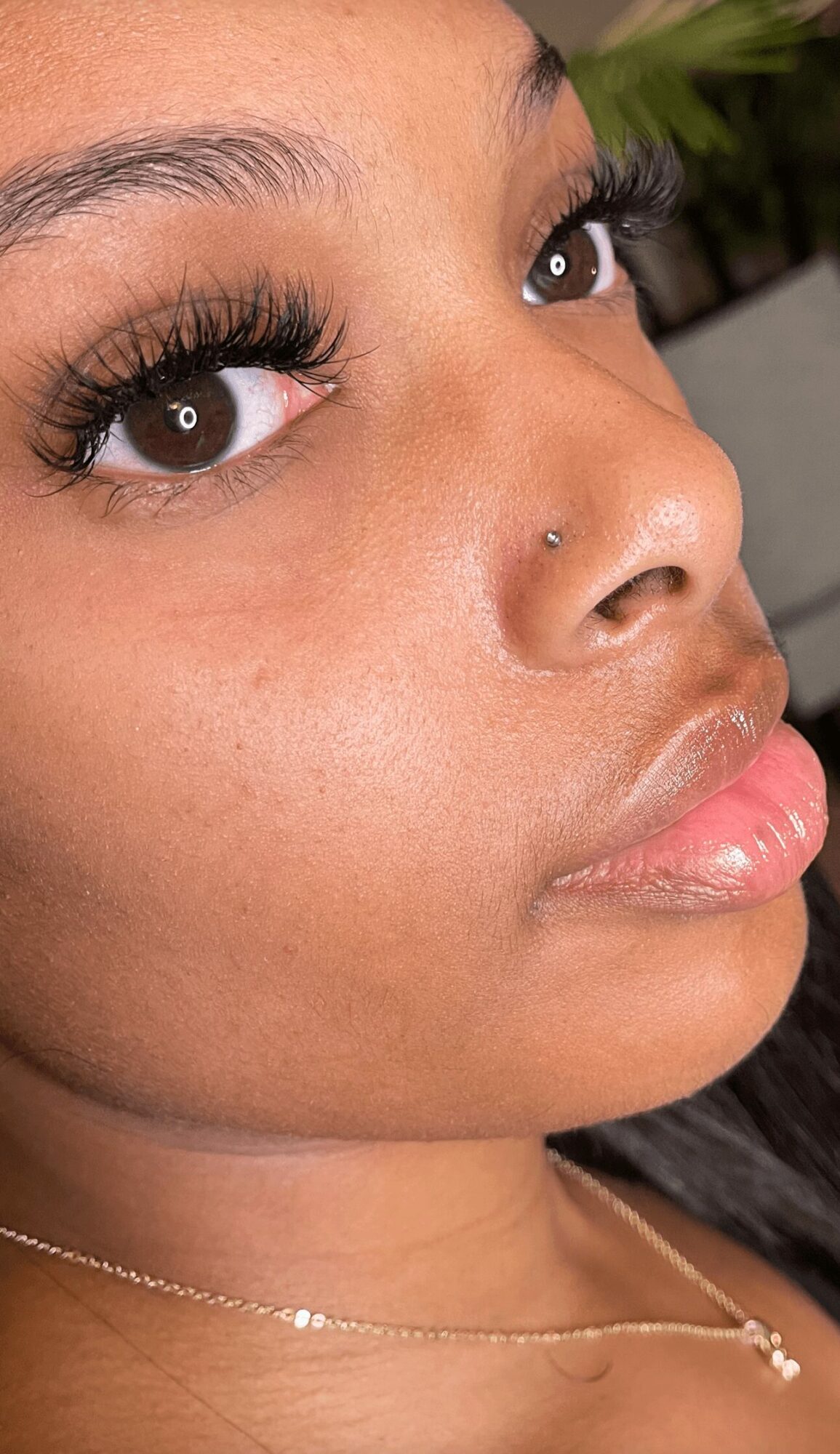 Close-up of a woman's face showing eyes, nose, and lips with makeup and a nose piercing.