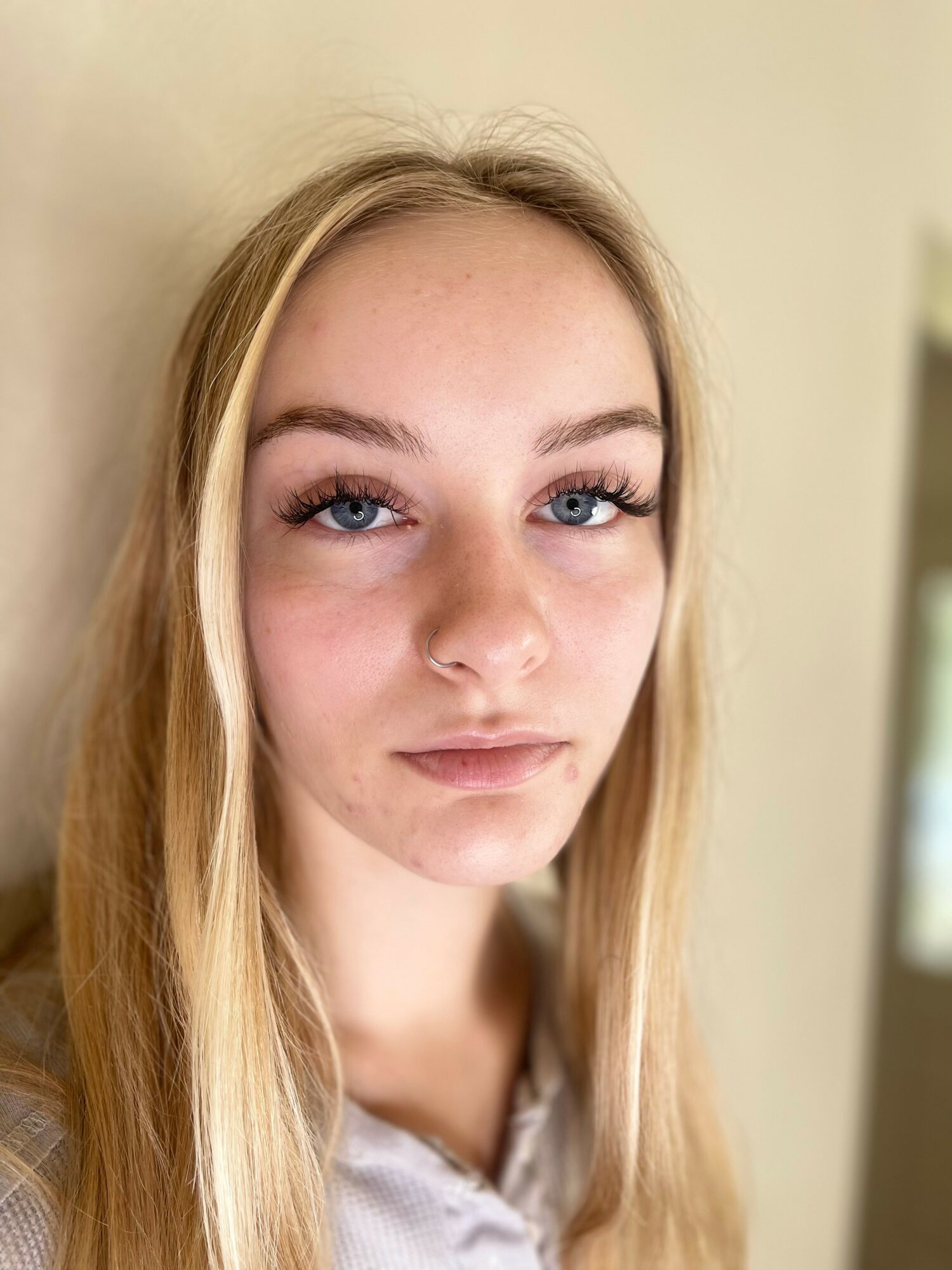 Young woman with long blonde hair and blue eyes looking at the camera, neutral expression, beige background.