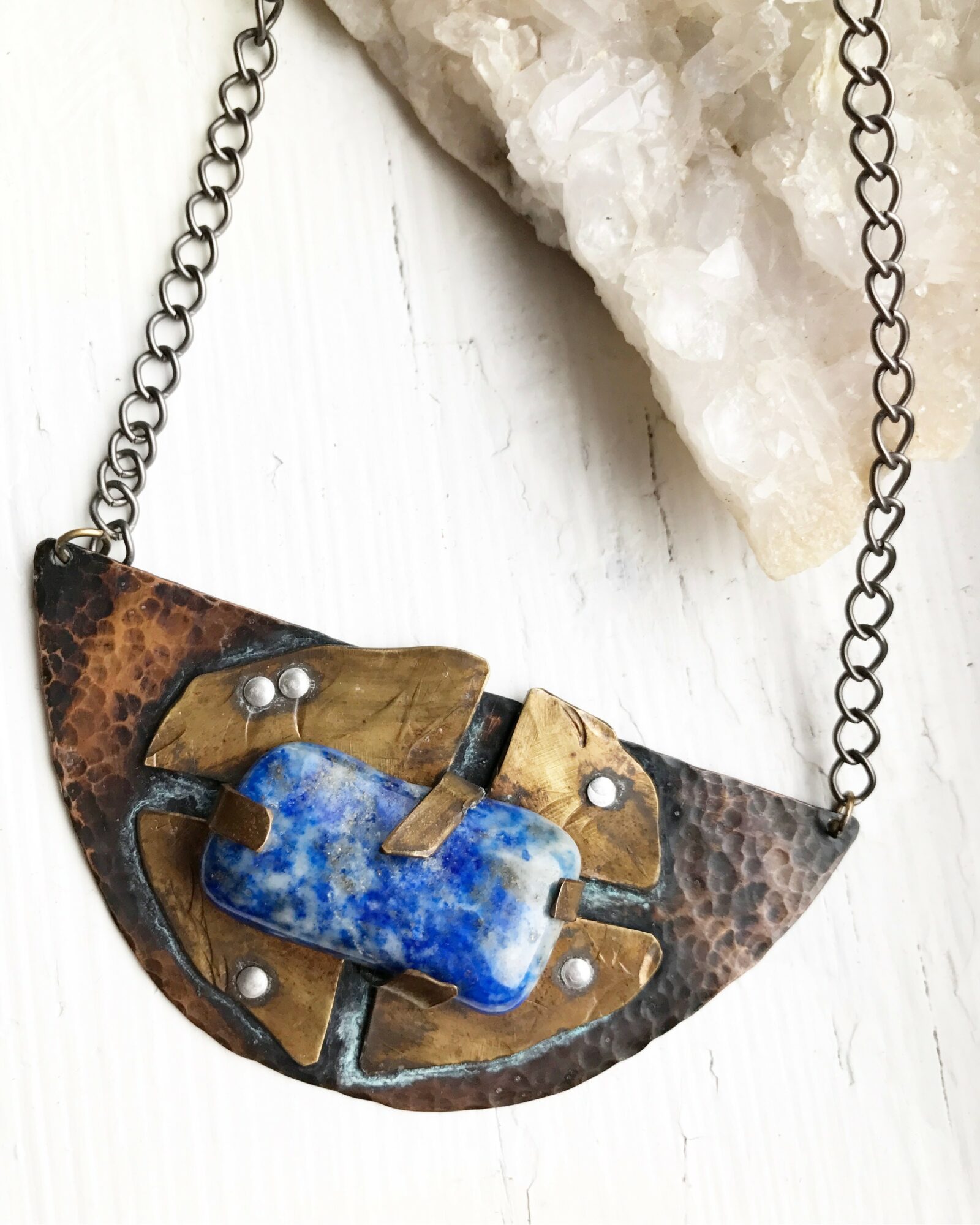Pendant necklace with a semi-circular metal piece, a blue stone, and small metal accents on a chain.