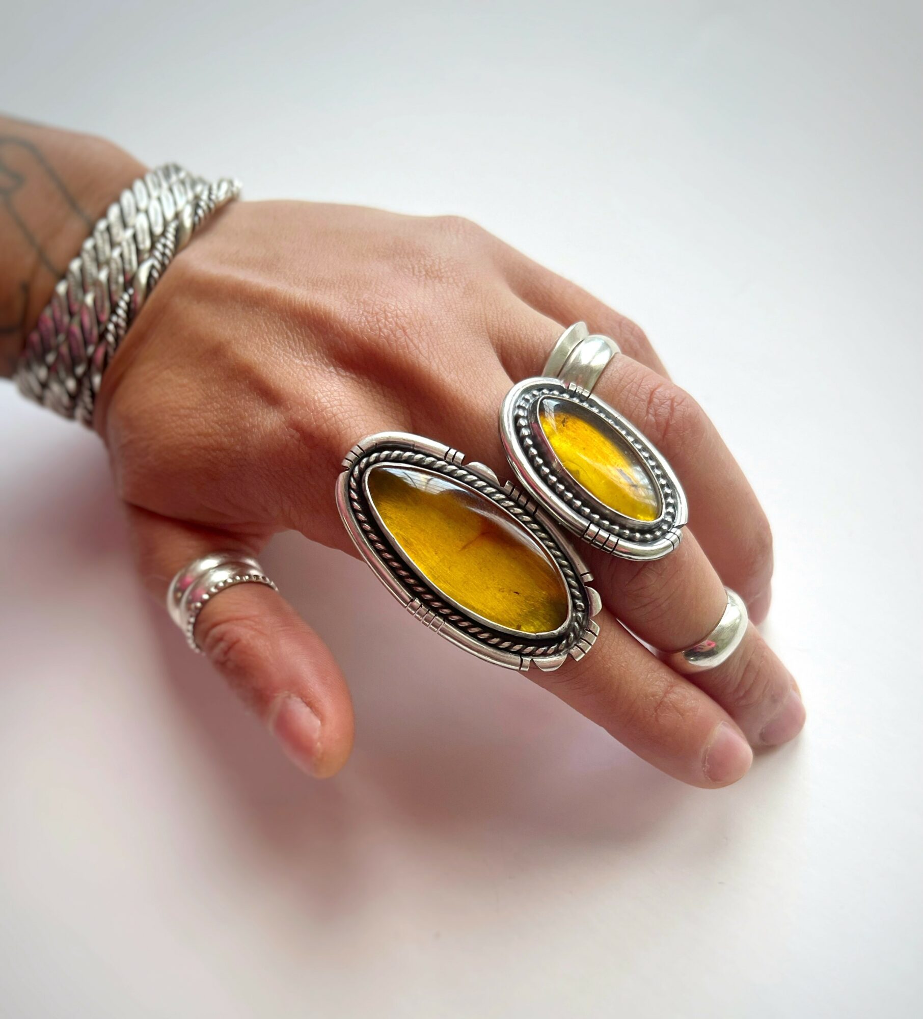 Hand with multiple rings and bracelets, featuring two large oval yellow stones in silver settings, on a white background.