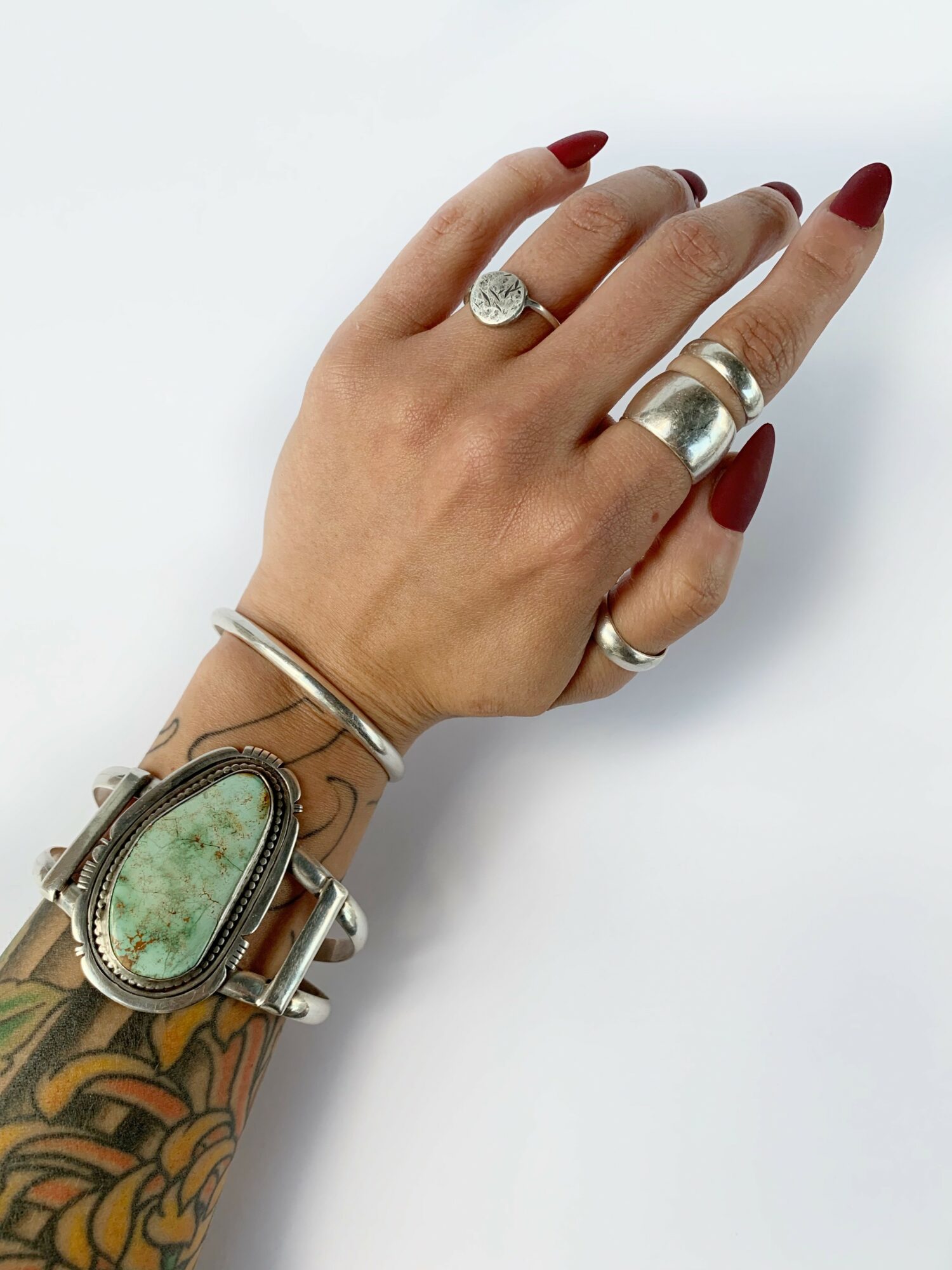 Hand with rings and a large watch, decorated with tattoos, against a white background.