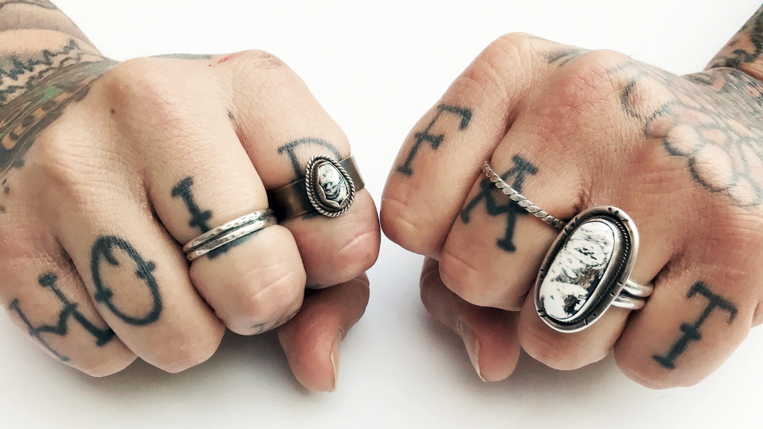 Two clenched fists with tattoos and rings, showing knuckles with the word 'LOVE' tattooed on fingers.