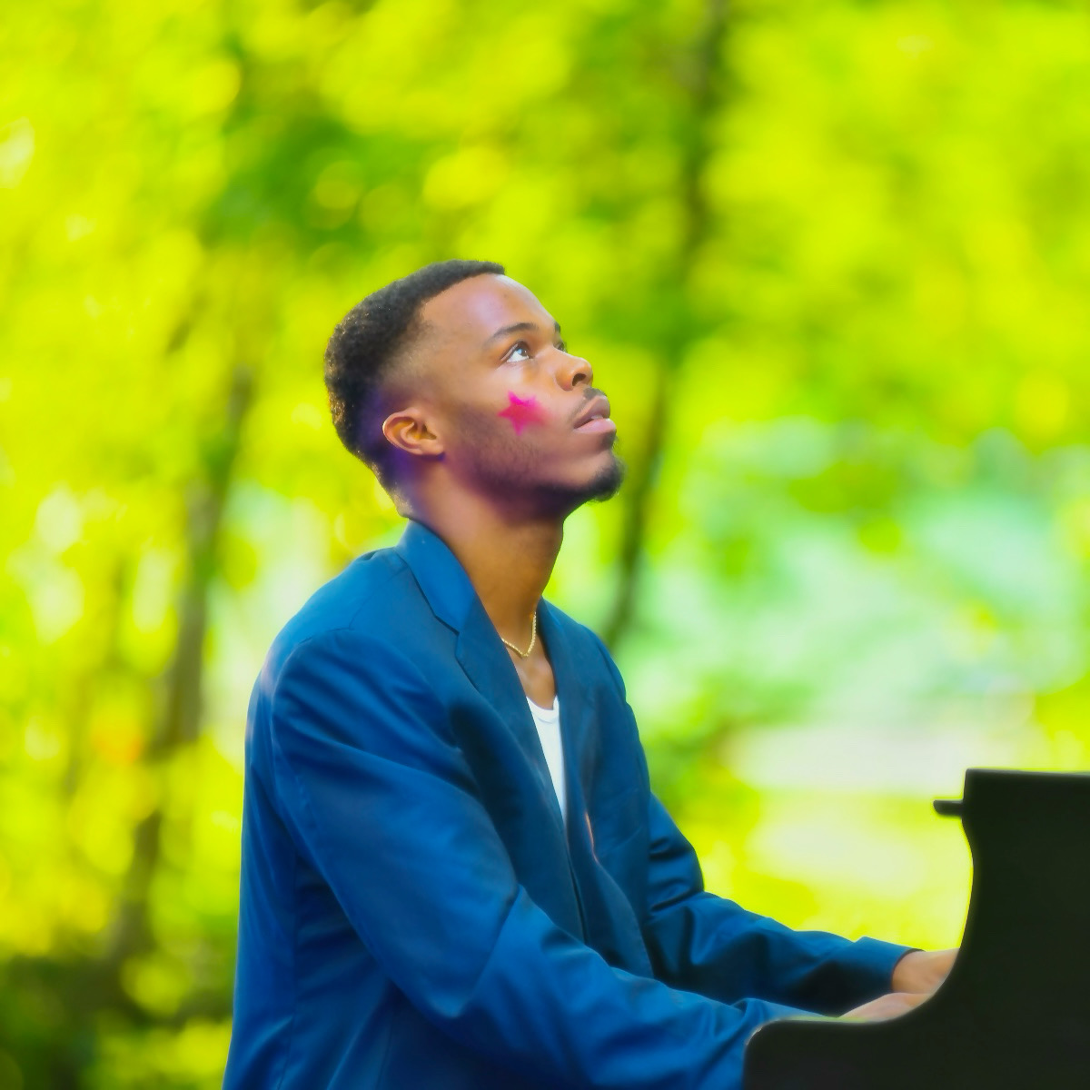 Young person with short hair in a blue jacket looking upward outdoors, surrounded by green trees.