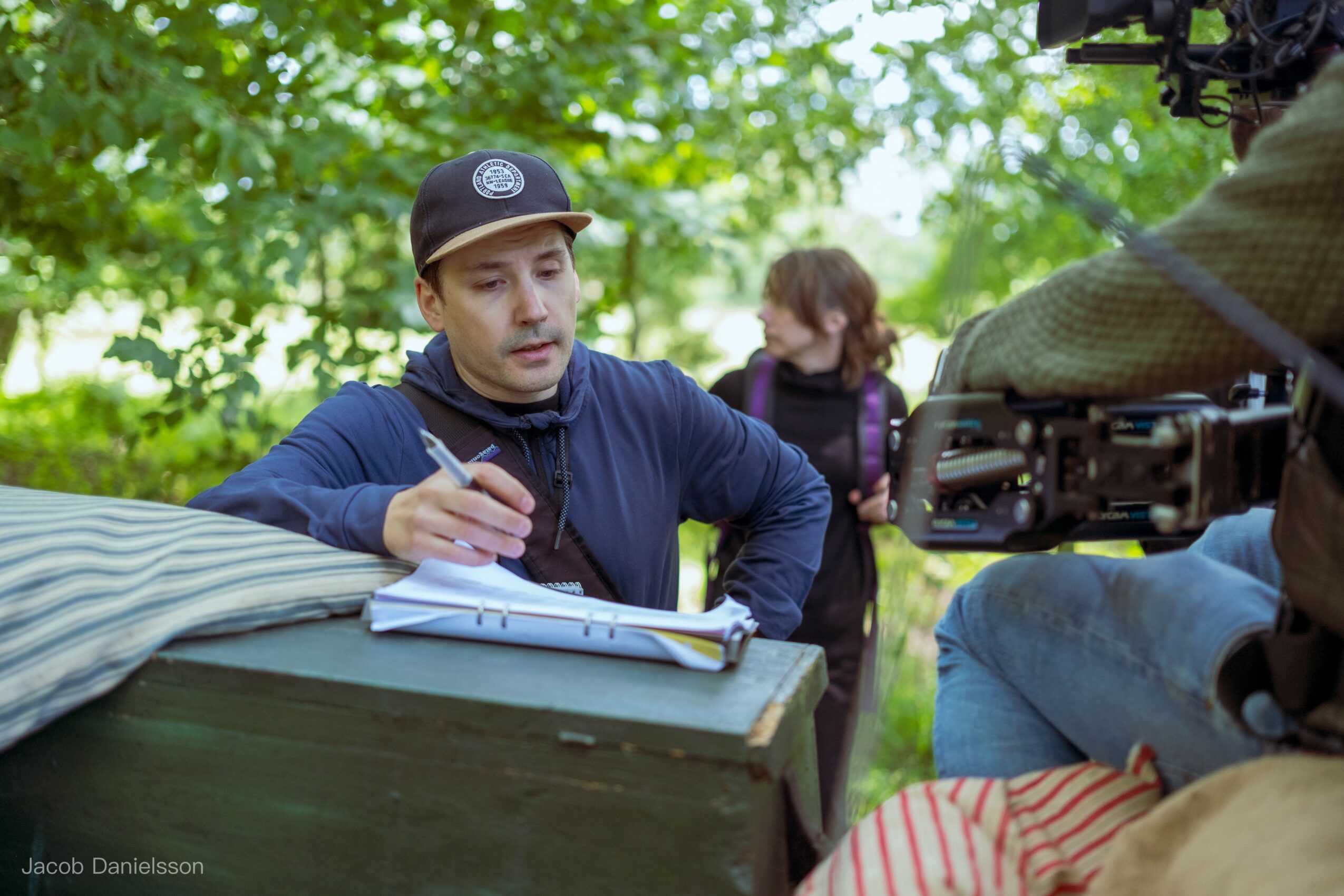Person signing autographs at an outdoor event with trees in the background.