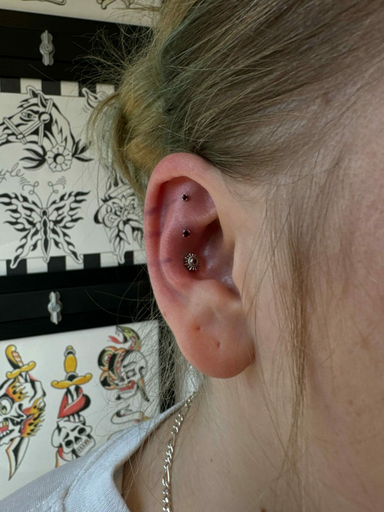 Close-up of a person's ear with multiple piercings and jewelry, and a background with cartoon characters.