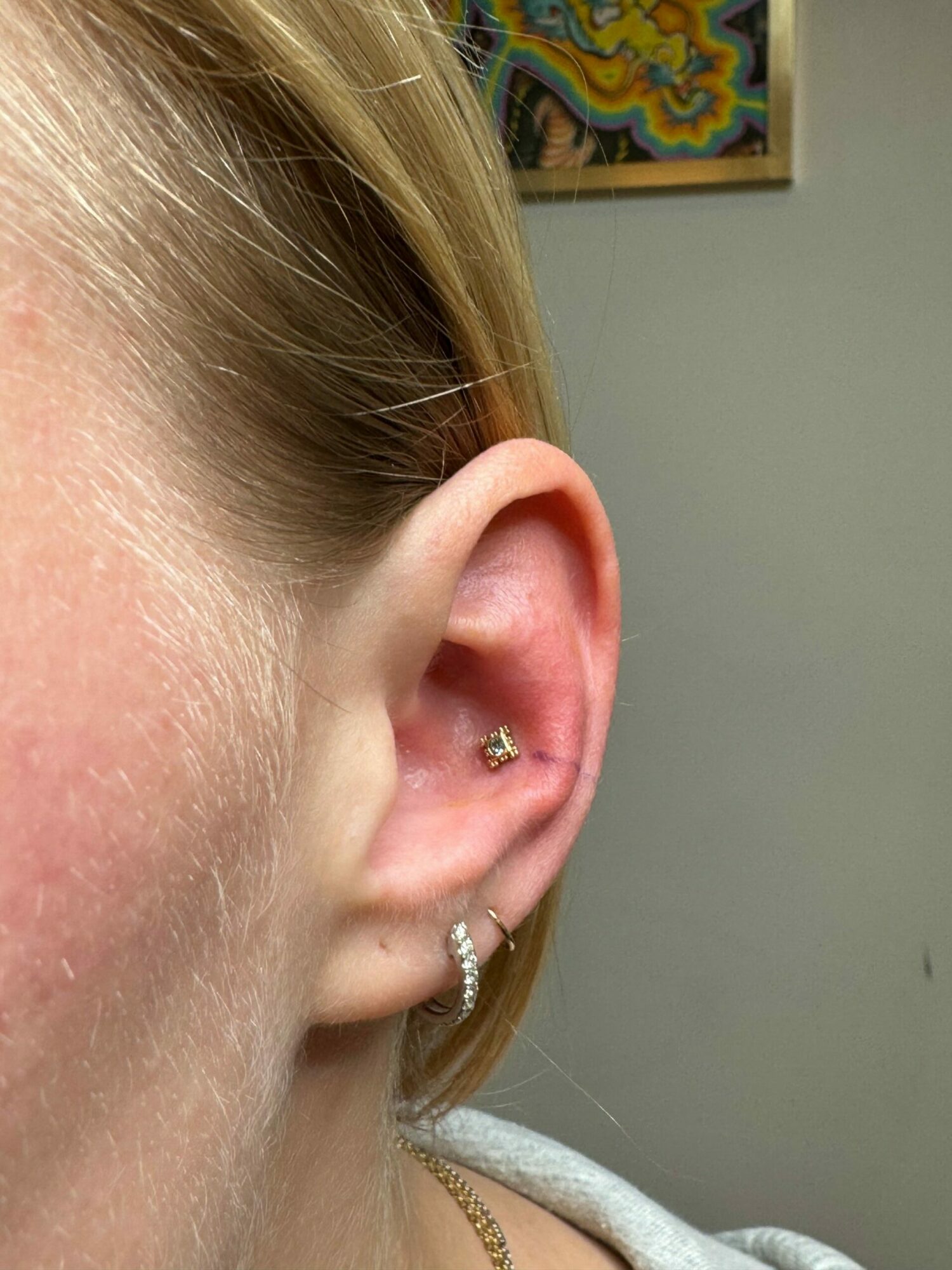 Close-up of a person's ear with multiple piercings, including a helix and lobe, against a plain background.
