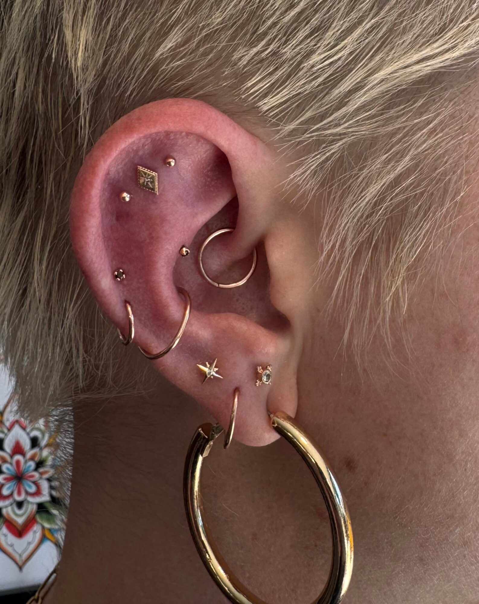 Close-up of a person's ear with multiple piercings and gold jewelry, including hoops and studs.