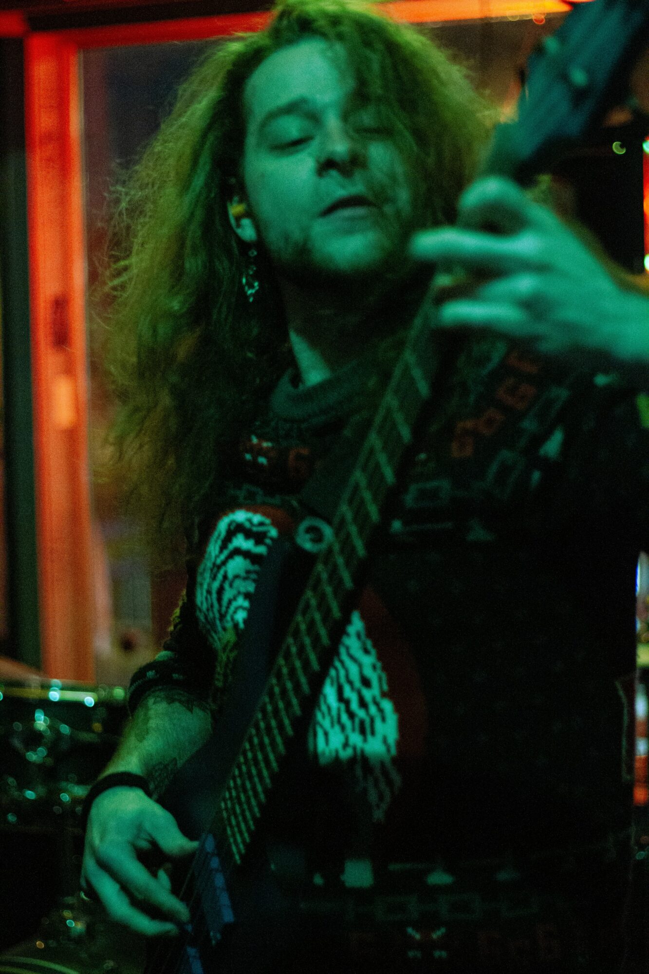 Person with long hair playing guitar in a dimly lit room with colorful lighting.