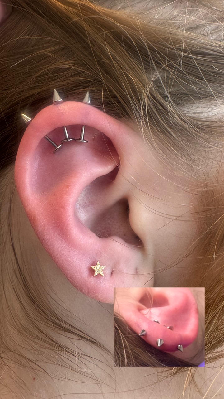 Close-up of a person's ear with multiple piercings, including a helix, tragus, and lobe, with a small star-shaped earring.