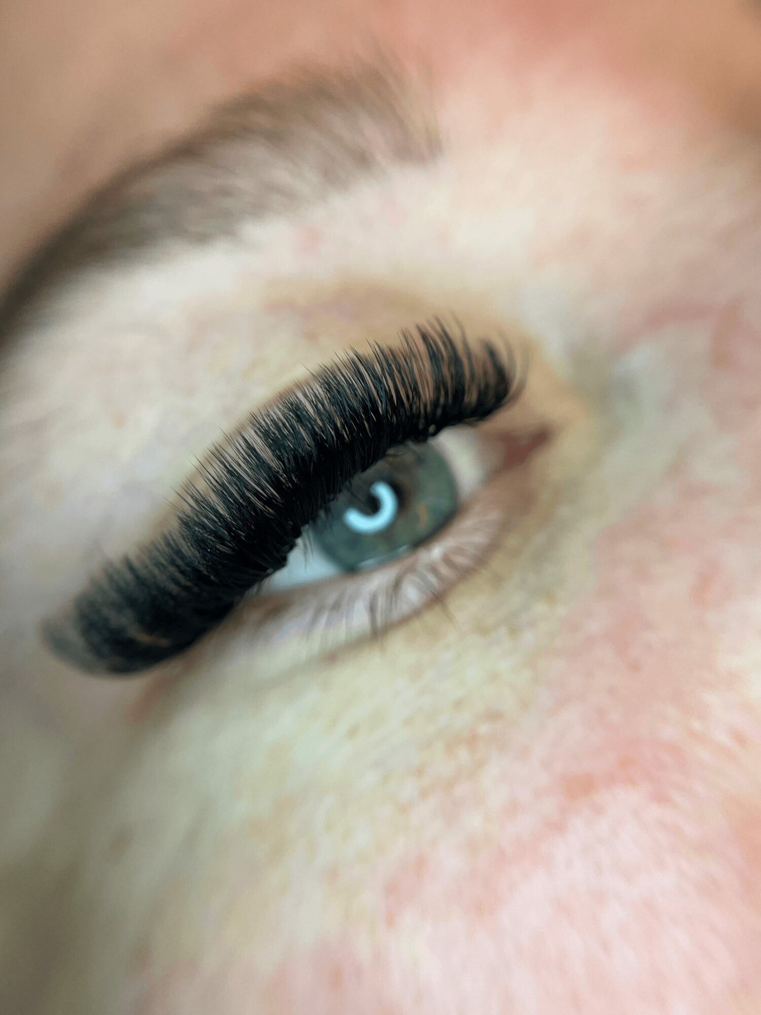 Close-up of a person's eye with long, dark eyelashes and a blue iris, showing skin texture and eyebrow hair.