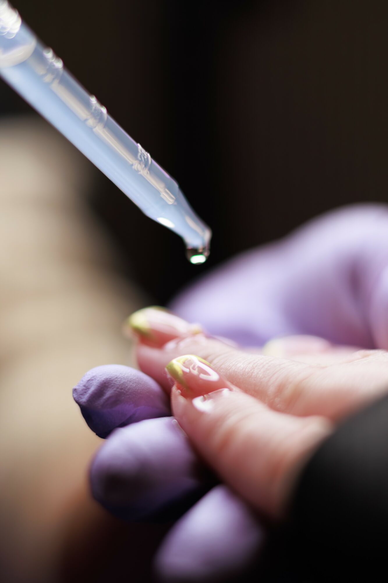 A close-up of a hand with purple gloves holding a finger, with a dropper above releasing a liquid onto the finger.