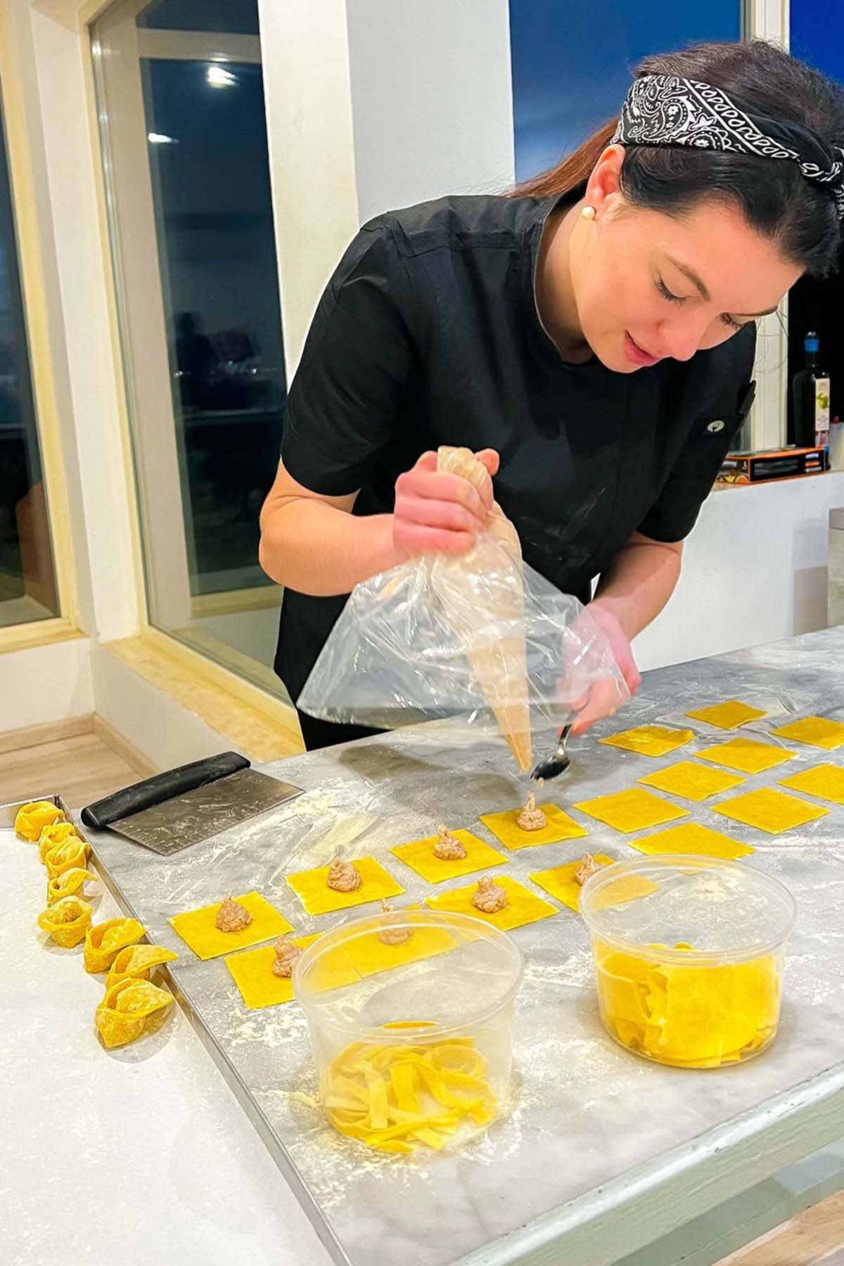 Woman in black shirt and headband piping yellow filling onto dough squares in a kitchen.