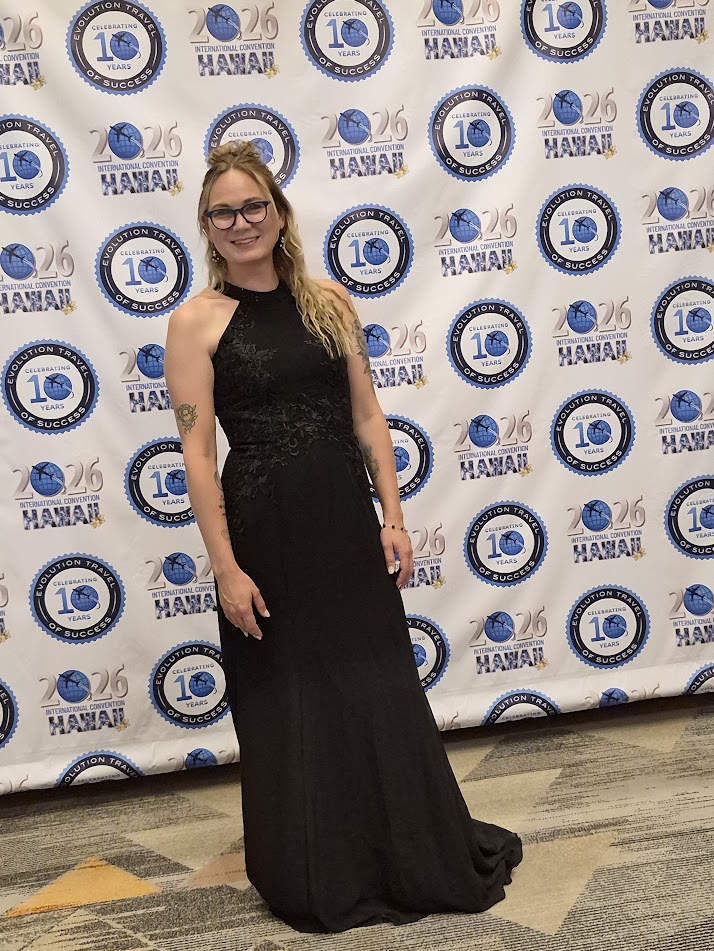 Woman in a black gown standing in front of a backdrop with blue and white logos and text, smiling.