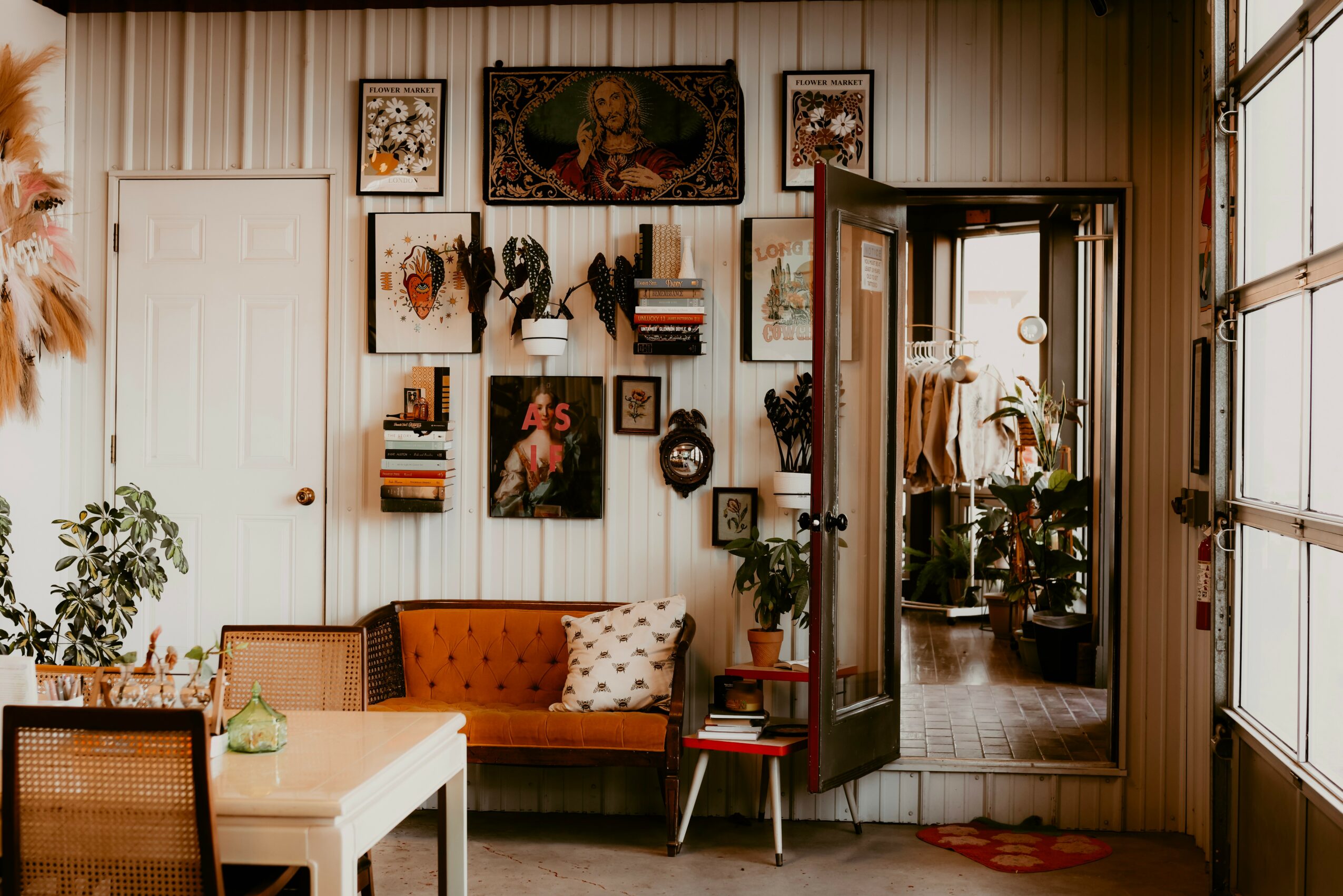 Interior of a room with a white wall decorated with framed pictures, a wooden door, a sofa with a pillow, and a glass cabinet.