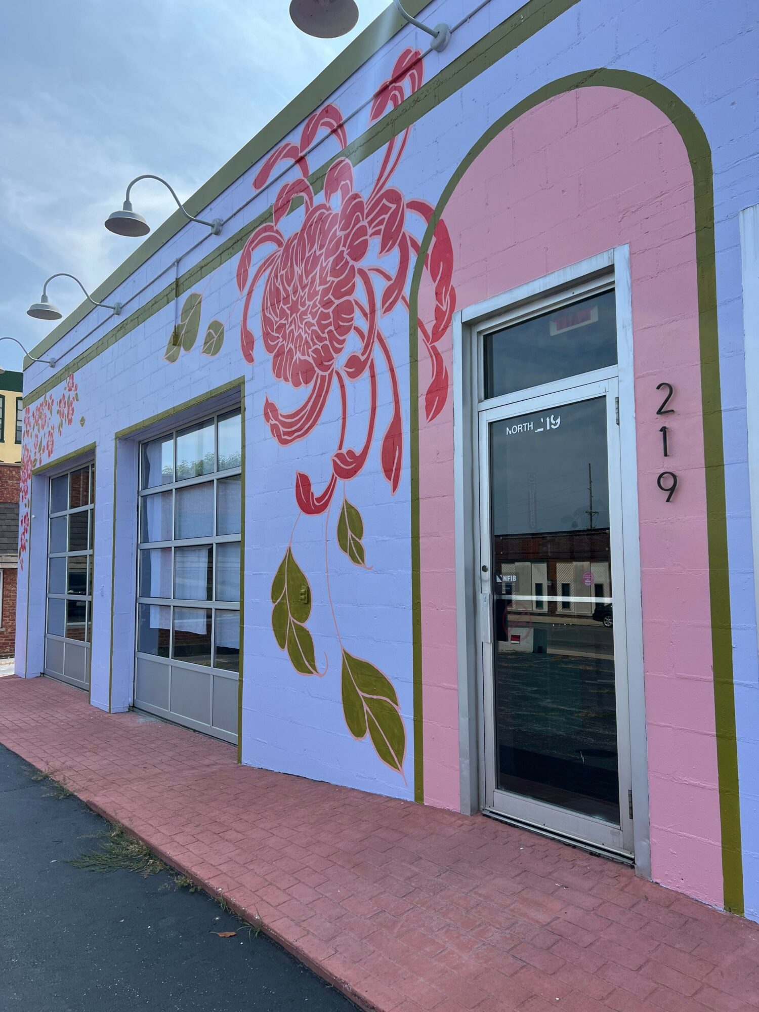 Colorful building with pink, purple, and green floral mural, windows, and a pink sidewalk.