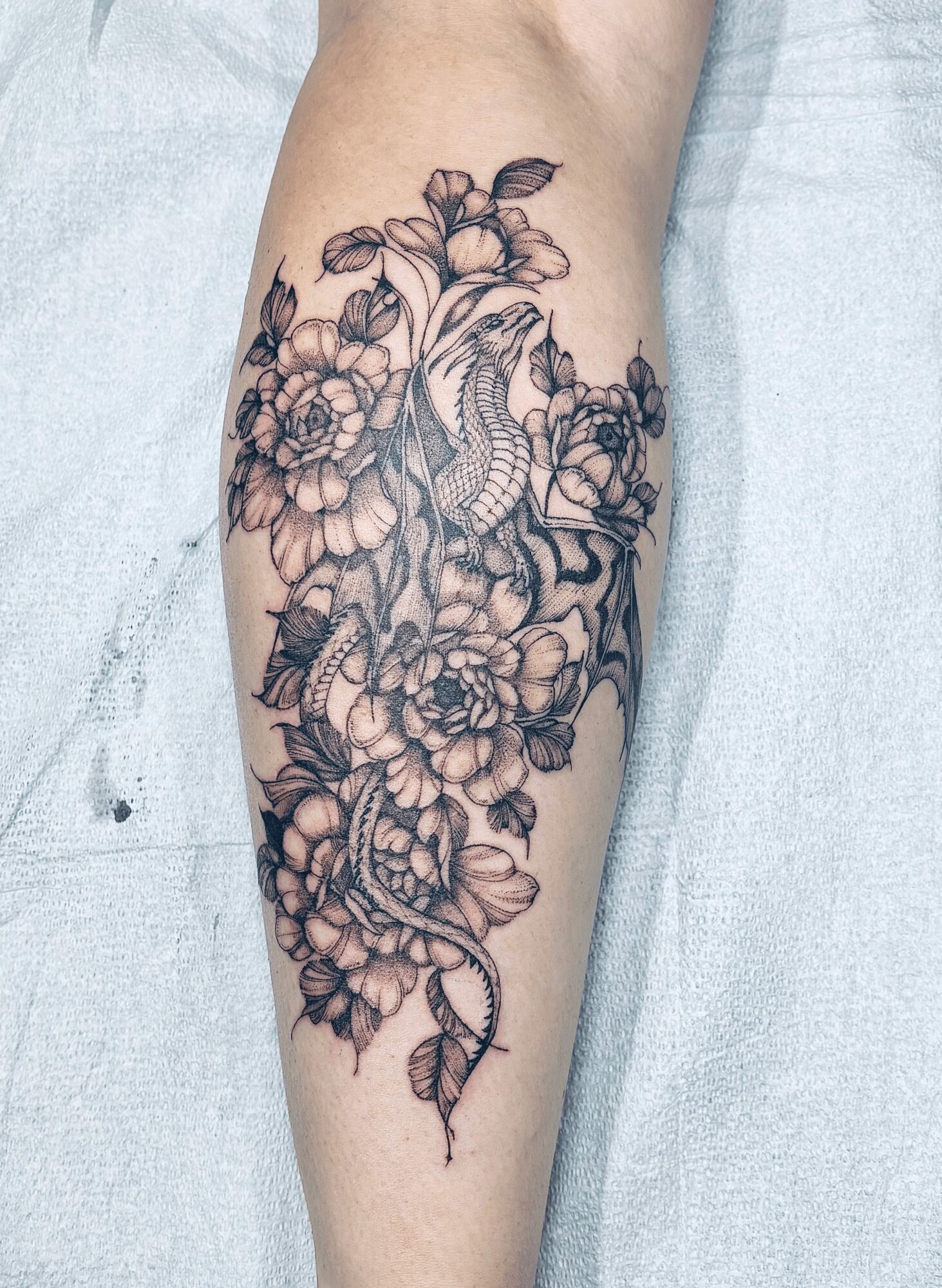 Tattoo of a snake intertwined with flowers on a person's forearm, detailed line work, black ink, floral design.