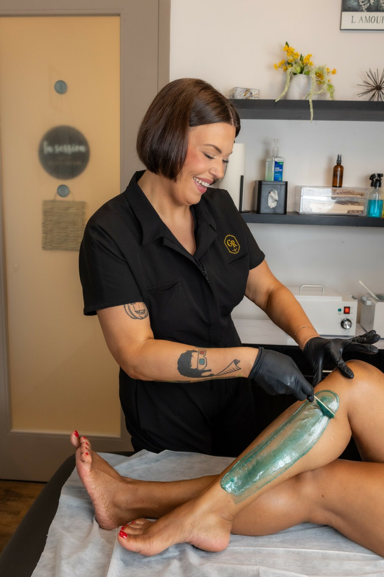 Woman with short dark hair smiling while applying a treatment to a person's leg in a clinic setting.
