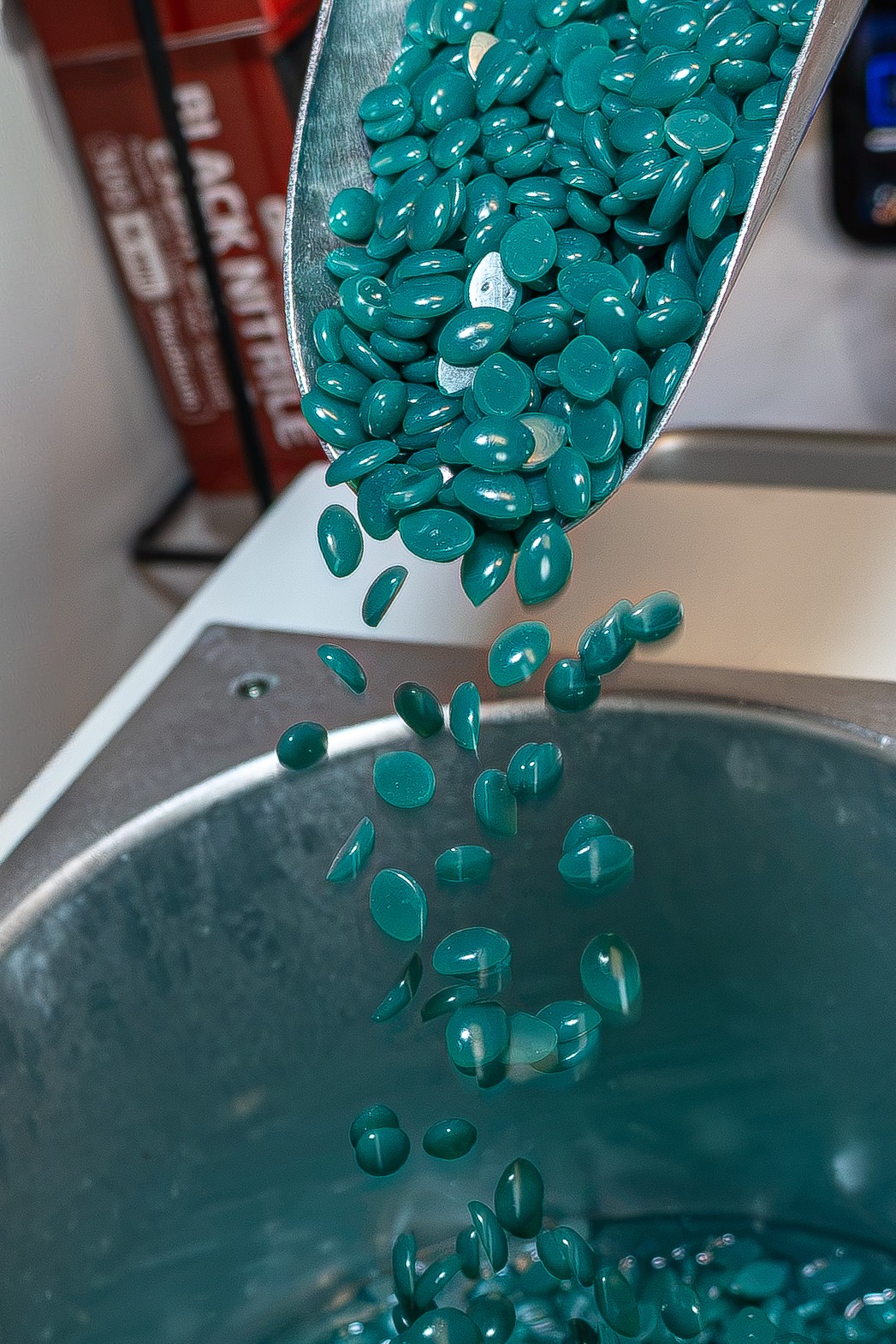 Blue pills are pouring from a container into a sink, with some pills mid-air. The sink is metallic and shiny.