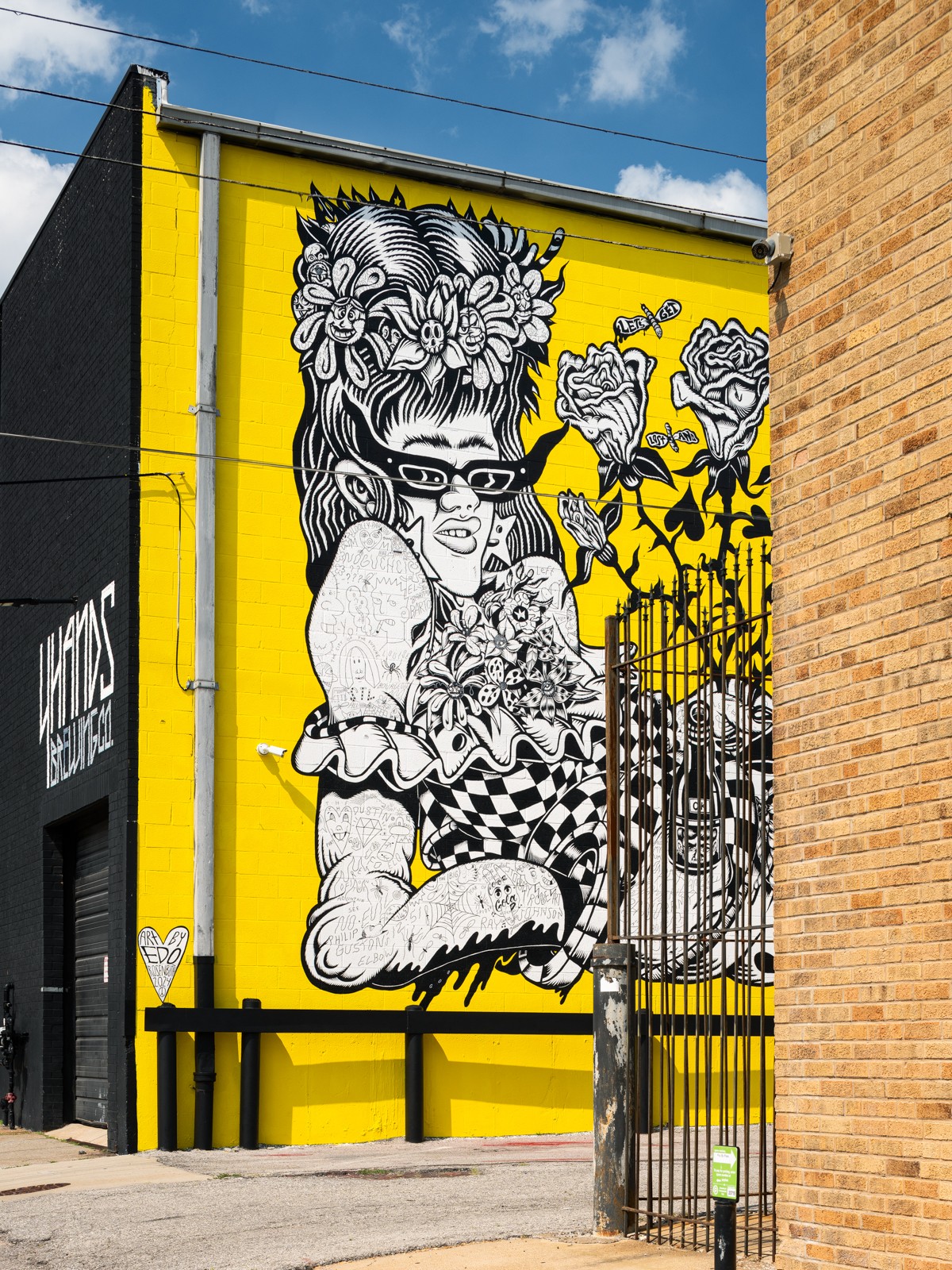 Black and white mural of a woman with glasses, floral hair, and tattoos on a yellow background.
