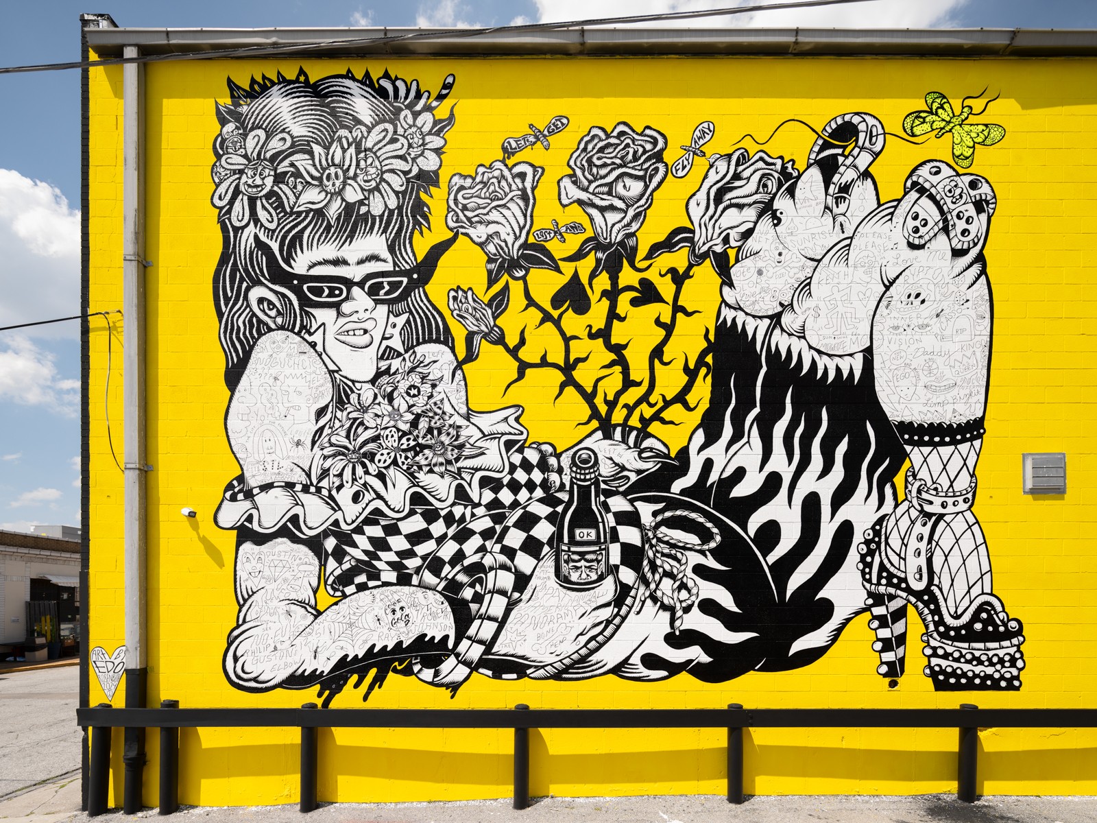 Black and white mural on yellow background featuring a girl with glasses, a cat, and various abstract elements.
