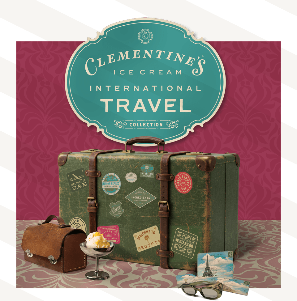 Travel-themed display with a suitcase, a small bag, a dessert, and a postcard in front of a pink background with a sign.