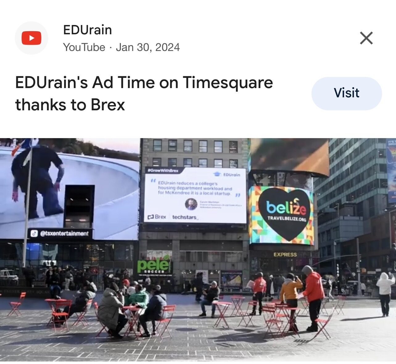 City square with people sitting and walking, large screens and colorful advertisements on buildings, outdoor seating area.