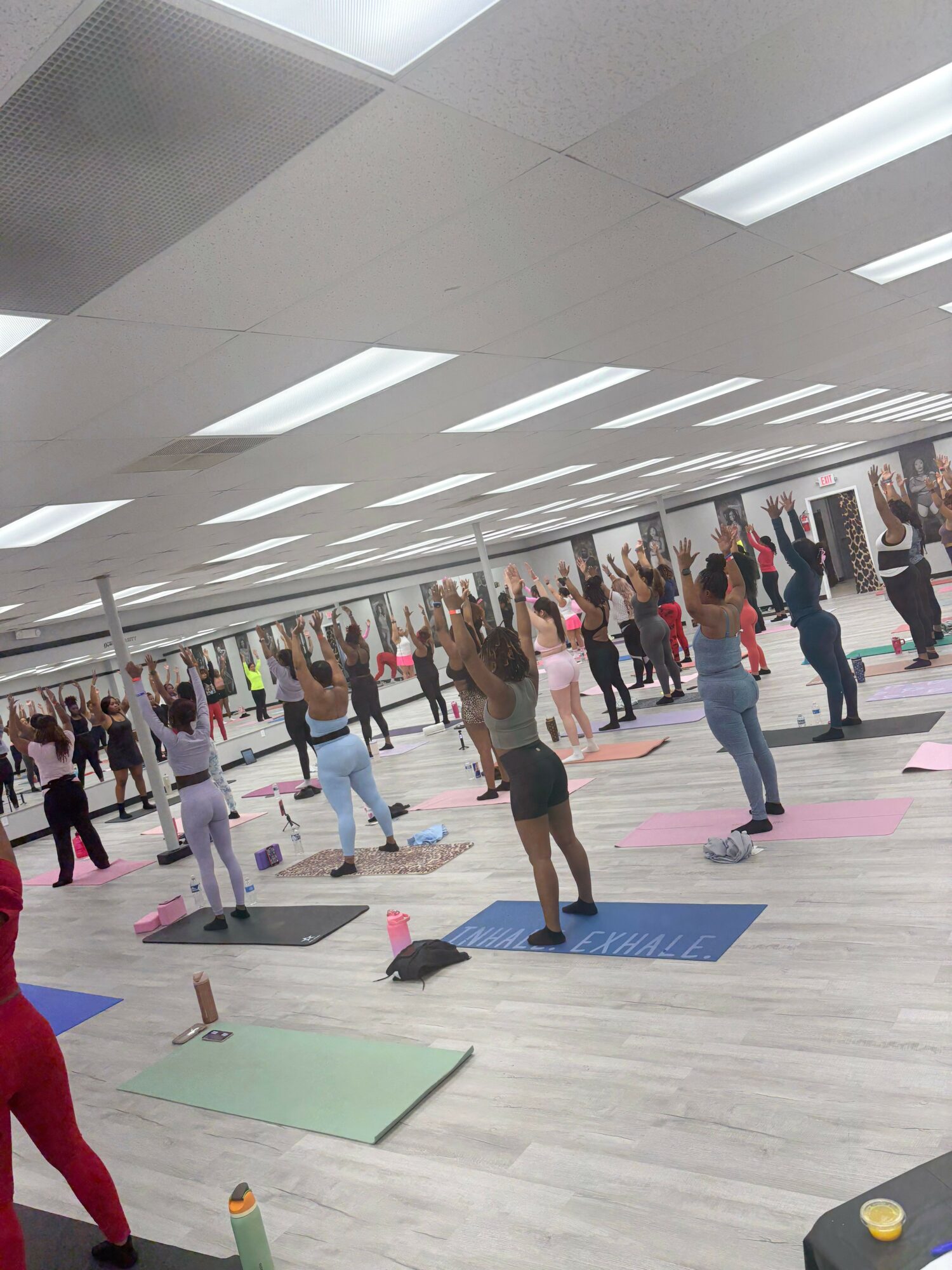 People practicing yoga on mats in a spacious indoor area with a crosswalk pattern on the floor.