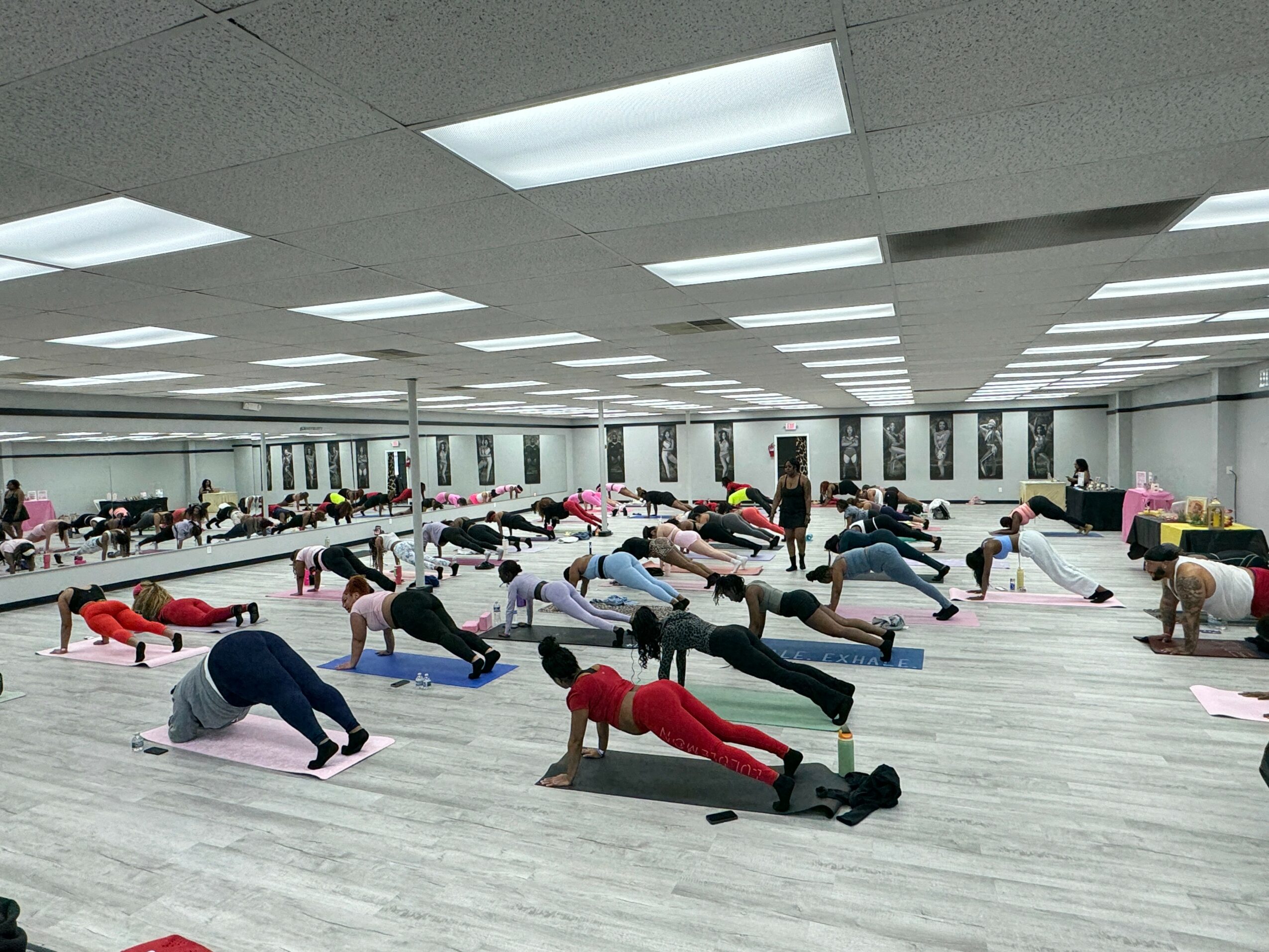 Group of people practicing yoga in a spacious studio with mirrors and bright ceiling lights.