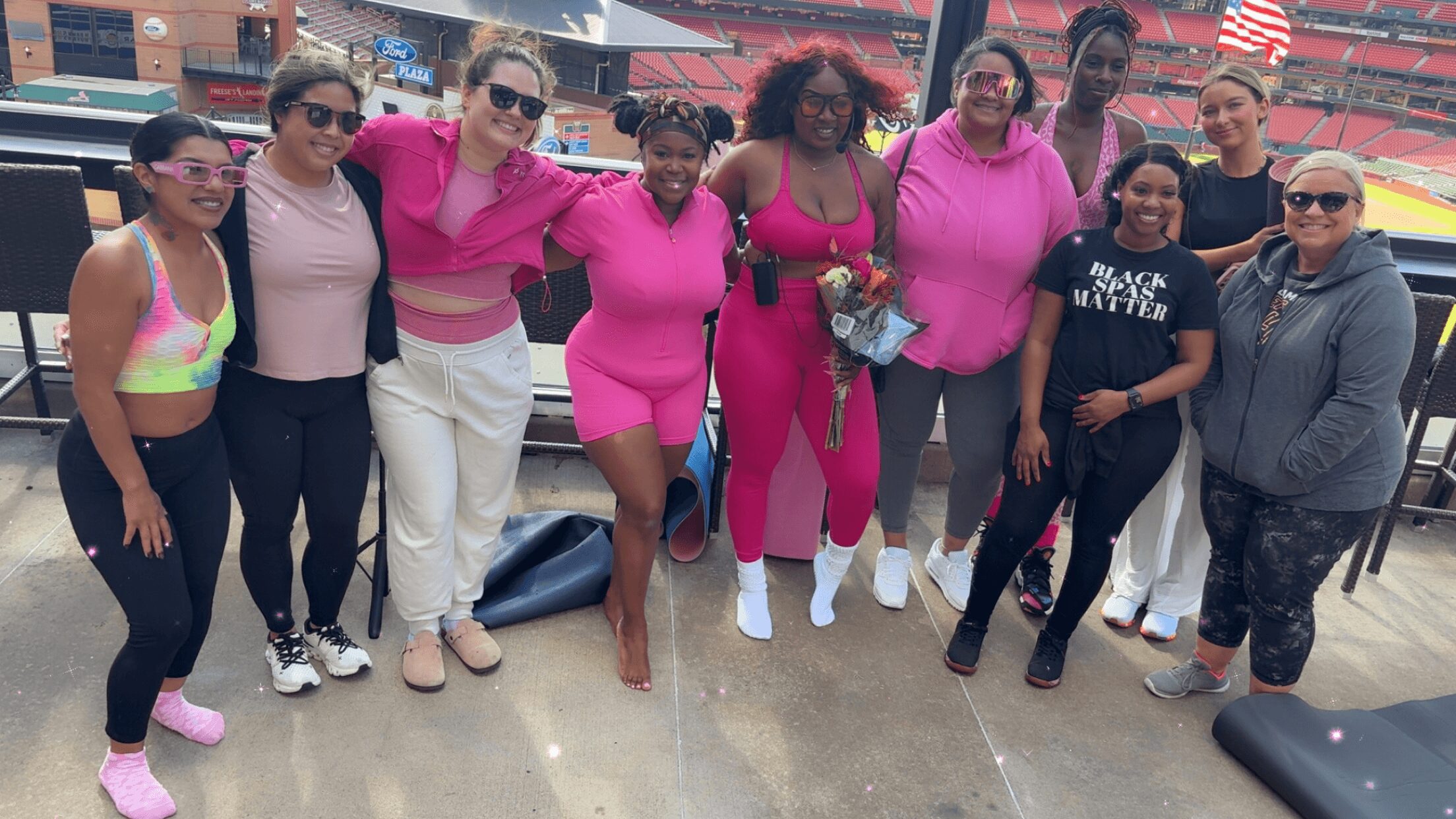 Group of women and girls standing together indoors, some holding bags, dressed in pink and casual clothing.