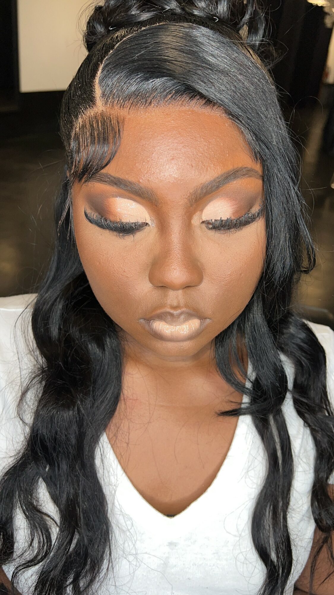Close-up of a woman with styled black hair, makeup, and closed eyes, wearing a white top.