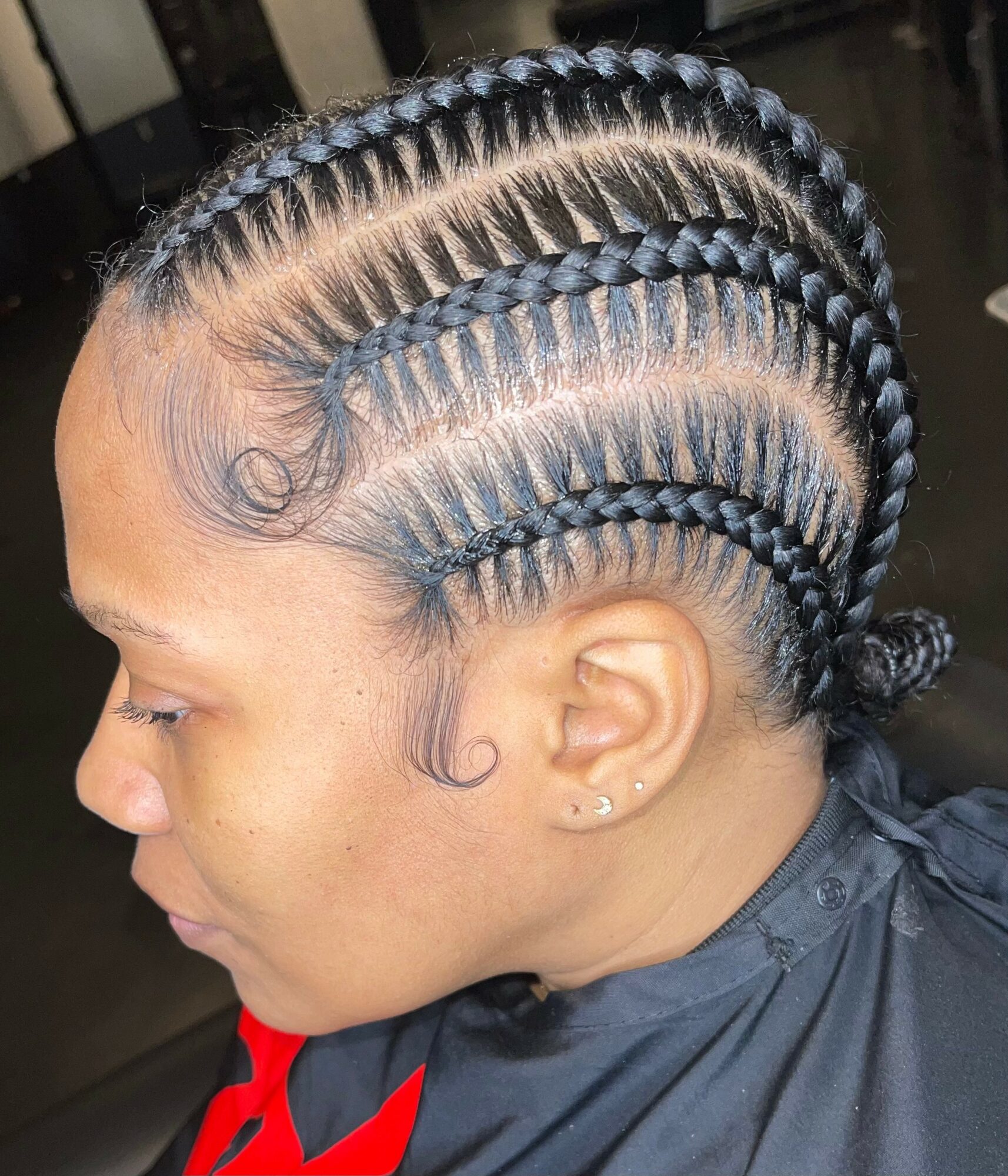 Side view of a woman with neatly braided hair styled in multiple cornrows, wearing a black cape with red accents.