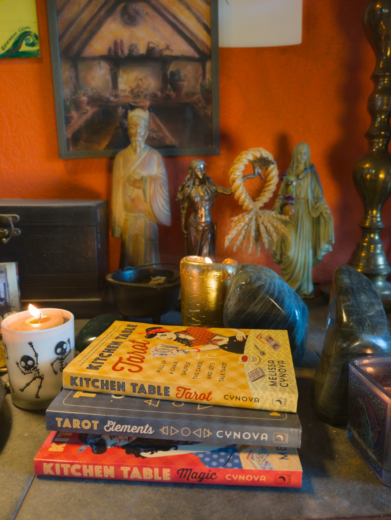 Shelf with candles, books, and decorative items against an orange wall, with a framed picture above. Word candles and figurines are visible.