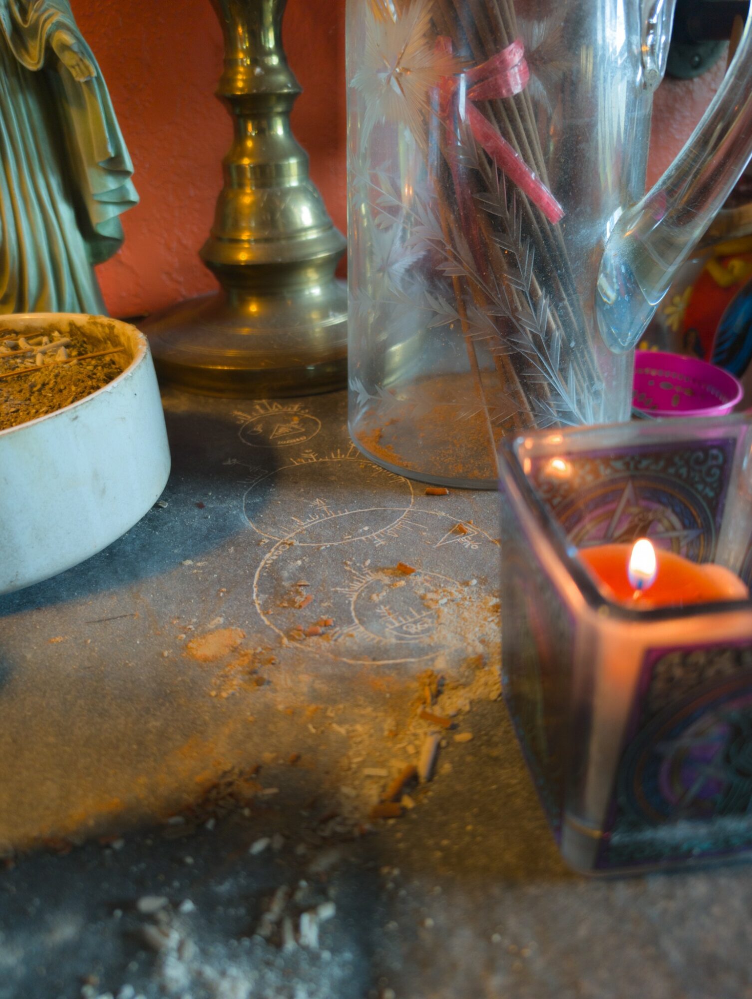 A cluttered surface with a candle, a glass pitcher, a pink container, and a small candle holder, with dust and debris.