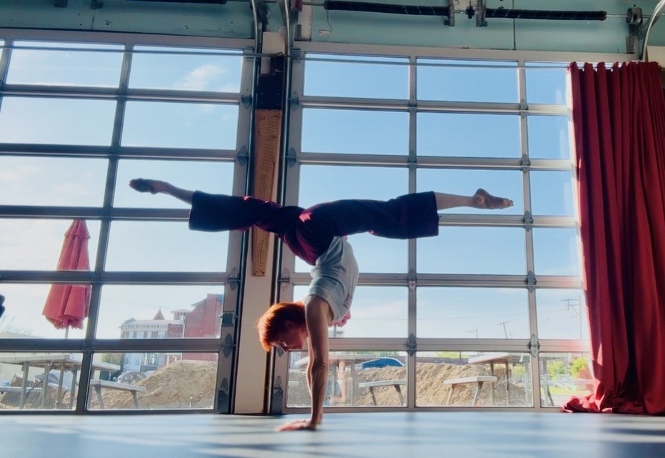 Person performing a handstand in front of large windows with a city view, red curtain on the right side.