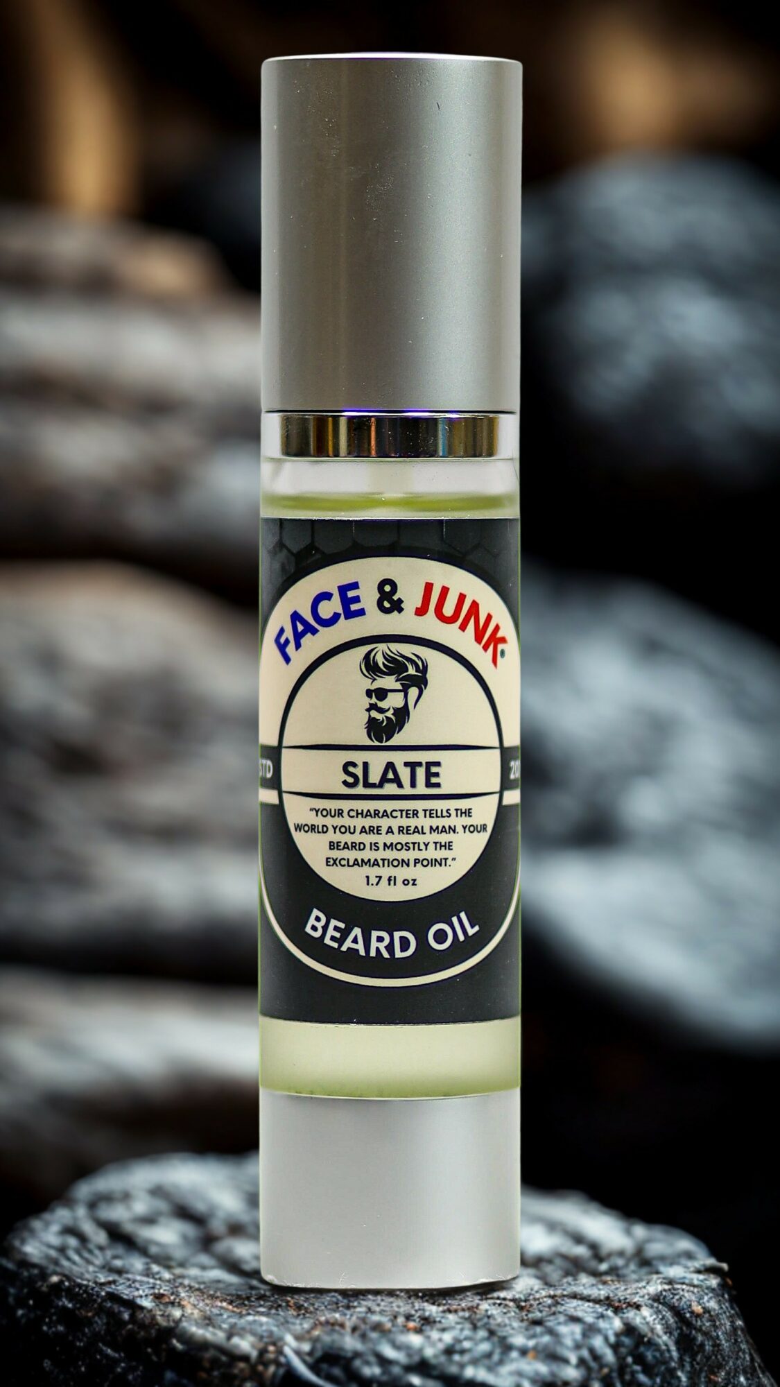 Beard oil bottle with label reading 'Face & Junk Slate Beard Oil' on a rock surface.