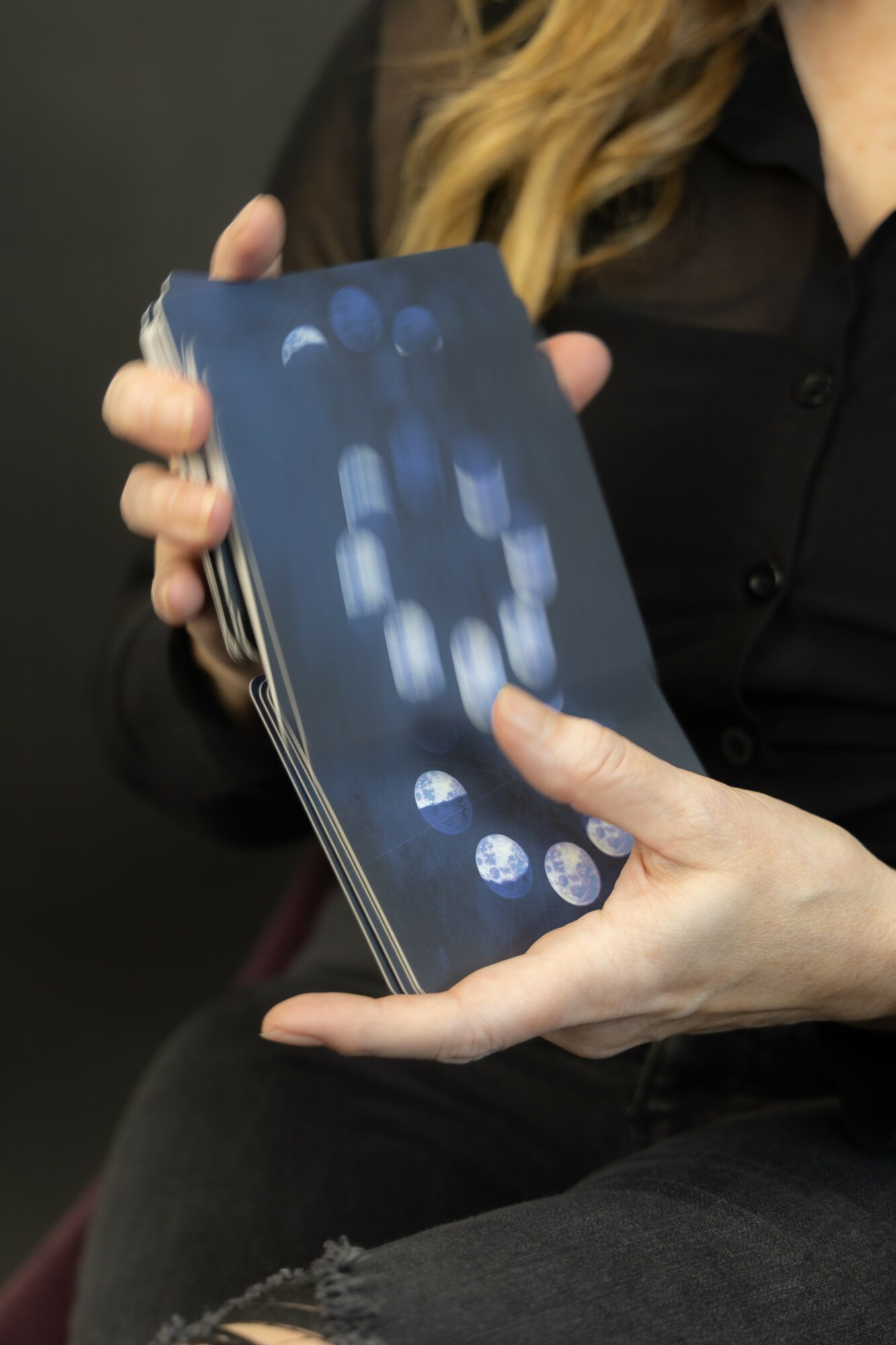Person holding a smartphone with a digital interface on the screen, fingers touching the screen, black clothing, blurred background.