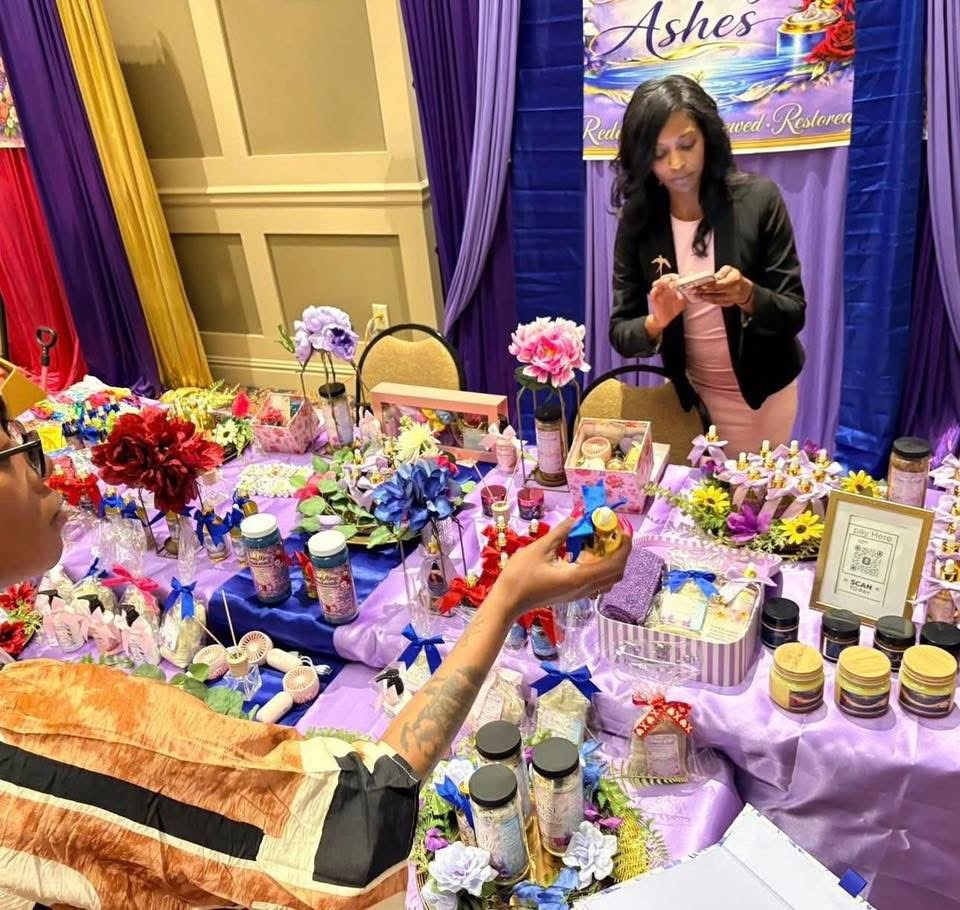 Woman browsing colorful products at a table with flowers and jars, in a decorated indoor setting.