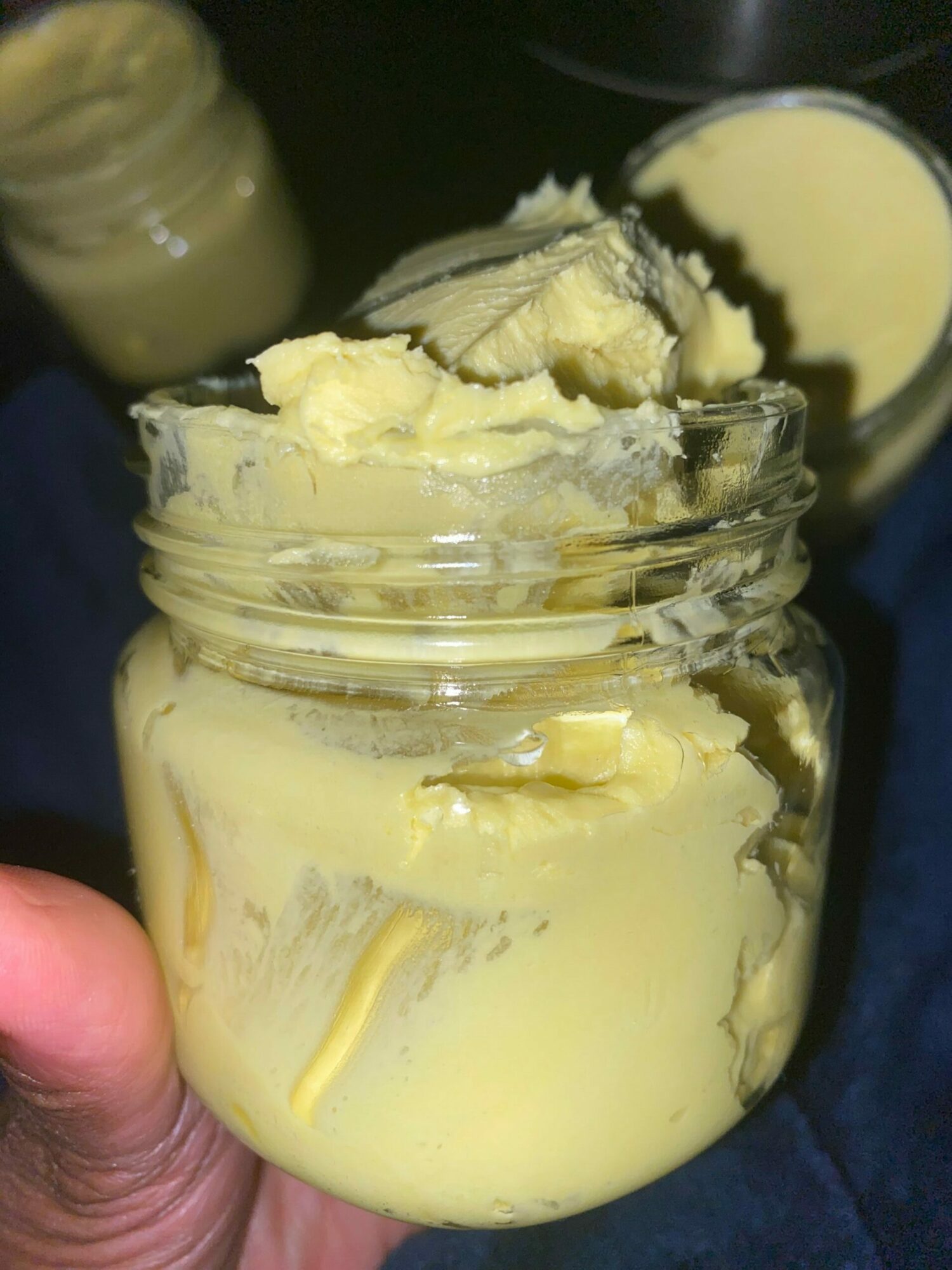 A jar of yellowish butter or margarine held in a person's hand, with a lid partially open.