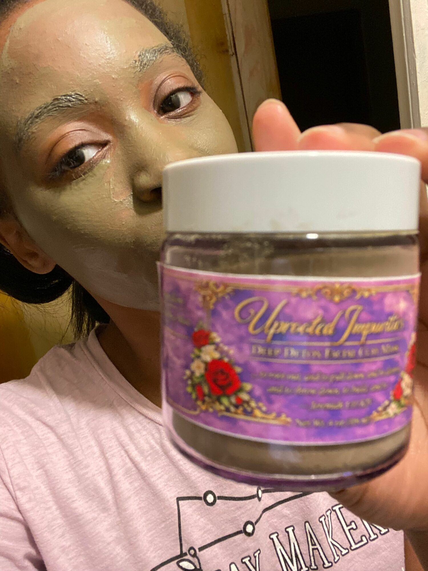Person with a green face mask holding a jar with a purple label and red flower, upside down.