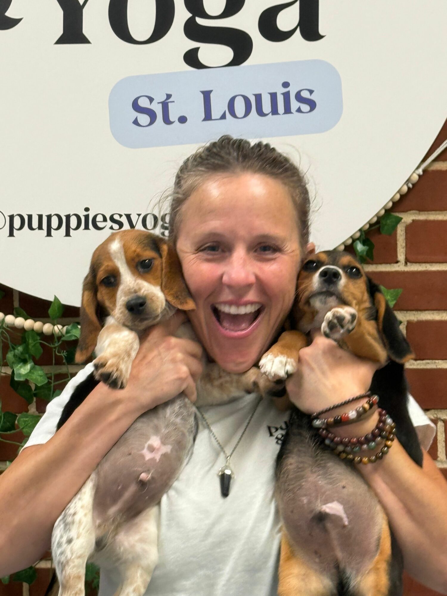 Woman holding two dogs, smiling, with a sign reading 'St. Louis' in the background.
