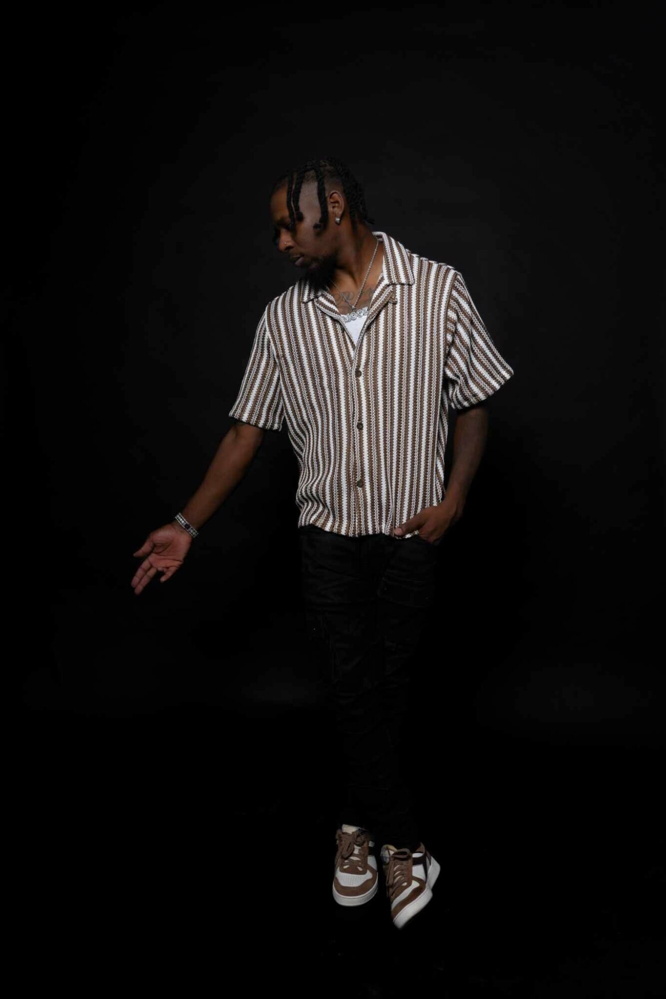 Person with striped shirt and sneakers standing against a dark background, looking down with one hand extended.