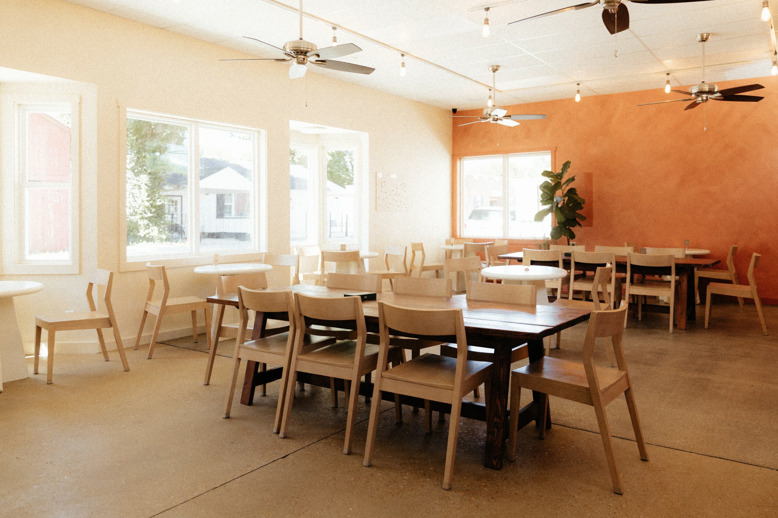 Dining area with tables and chairs, large windows, ceiling fans, and a pink accent wall, bright and airy space.