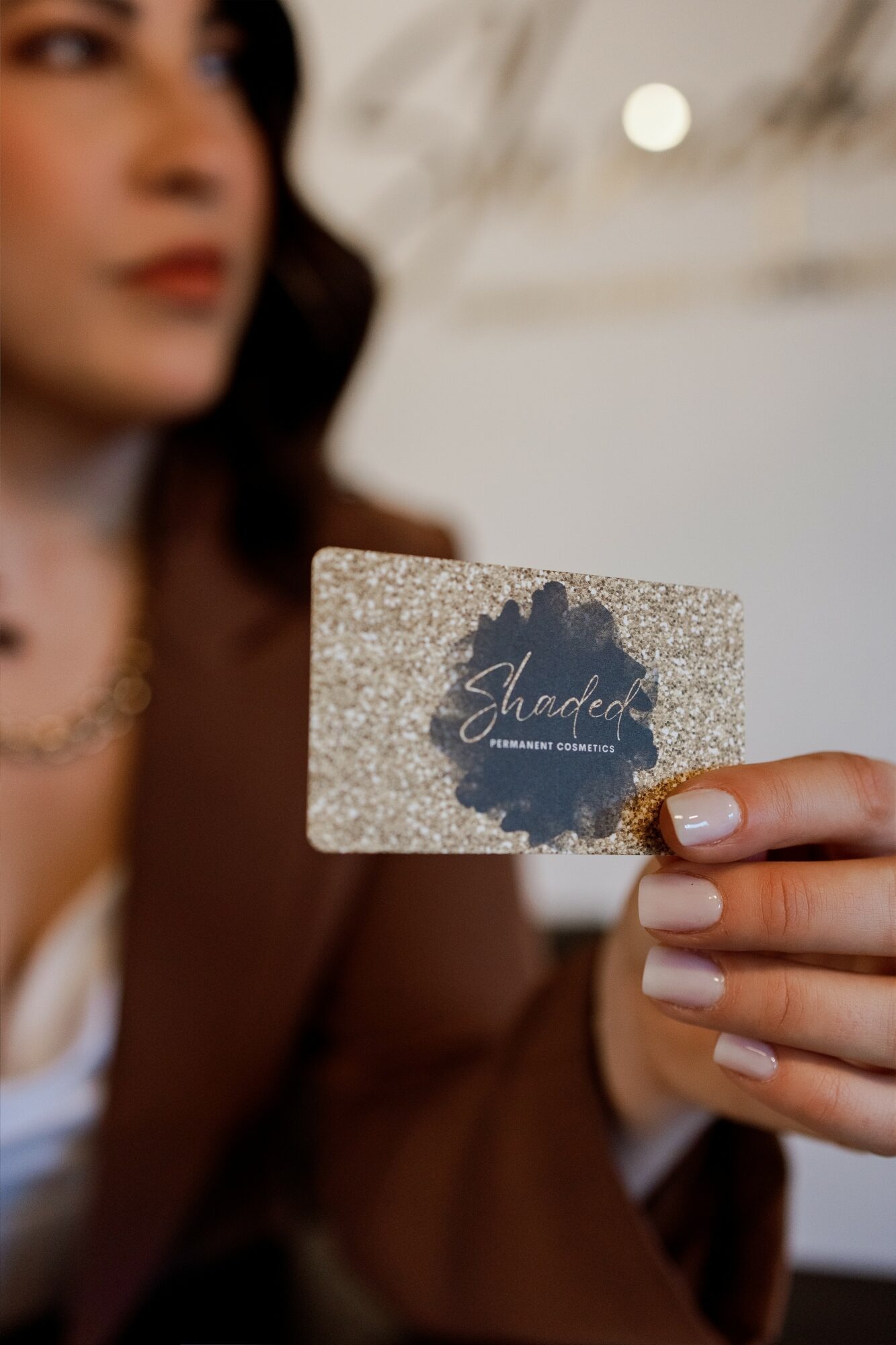 Person holding a glittery card with a dark ink splash and the word 'Shadeed' written on it, blurred background.