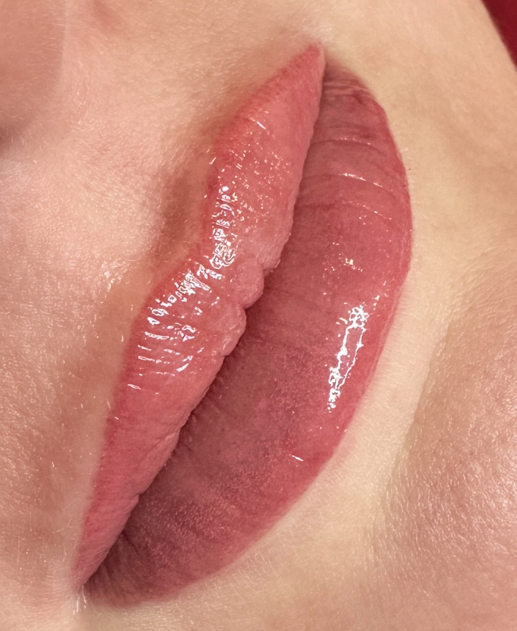 Close-up of lips with glossy, pinkish color, showing natural texture and shine.
