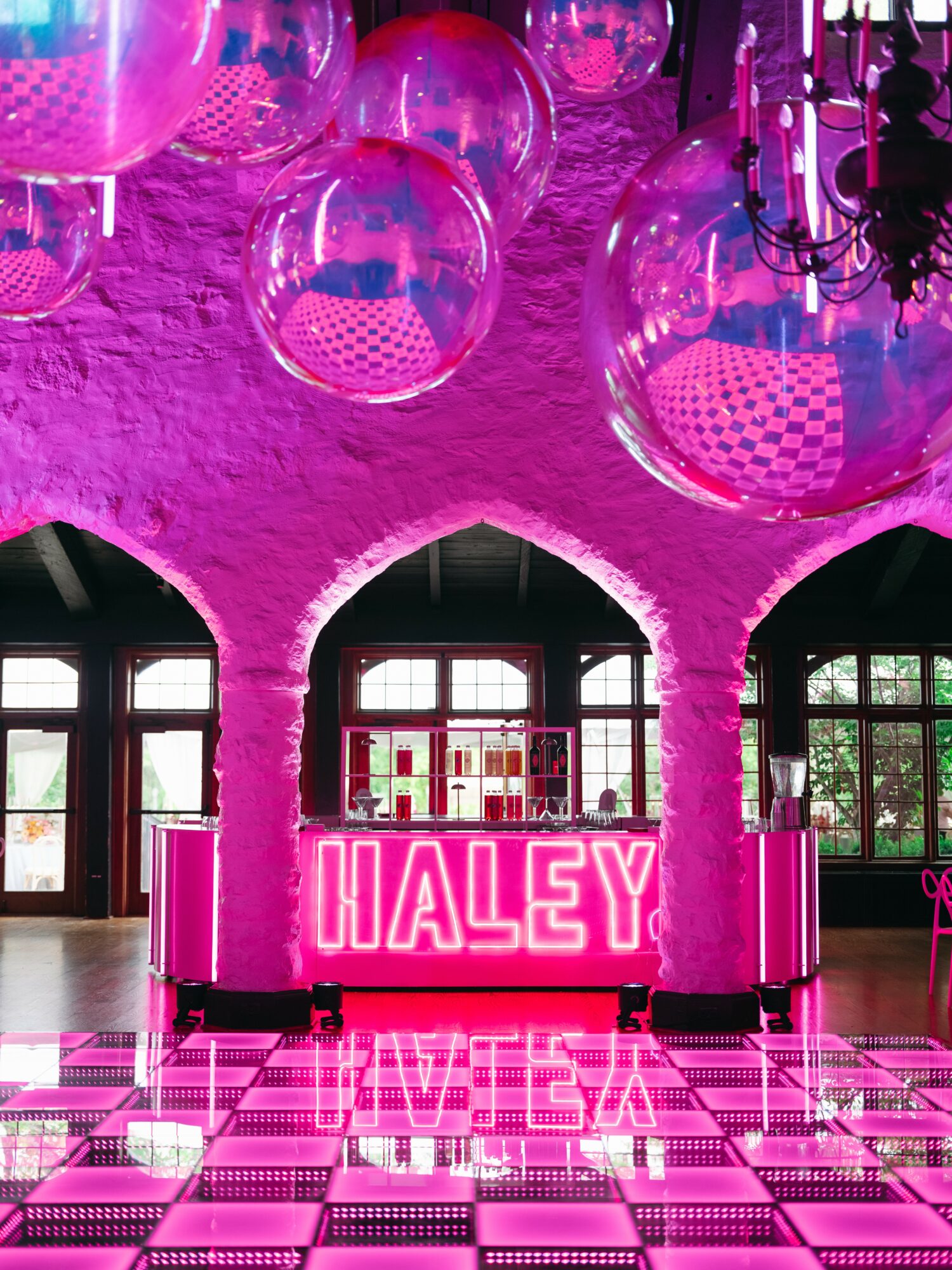 Interior with pink lighting, hanging transparent spheres, arched windows, and a neon sign reading 'HALEY' on a checkered floor.